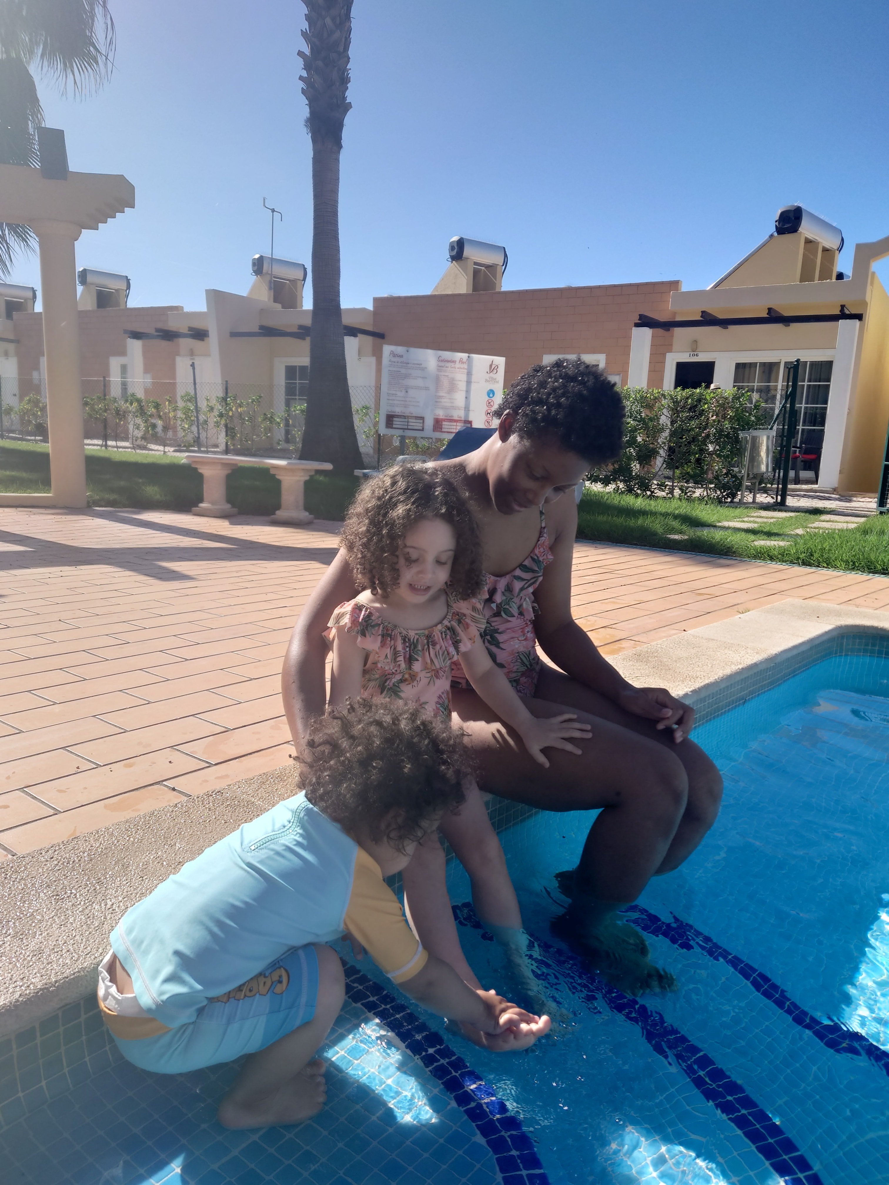 Advisor and two young children sitting poolside at a hotel resort on a sunny day