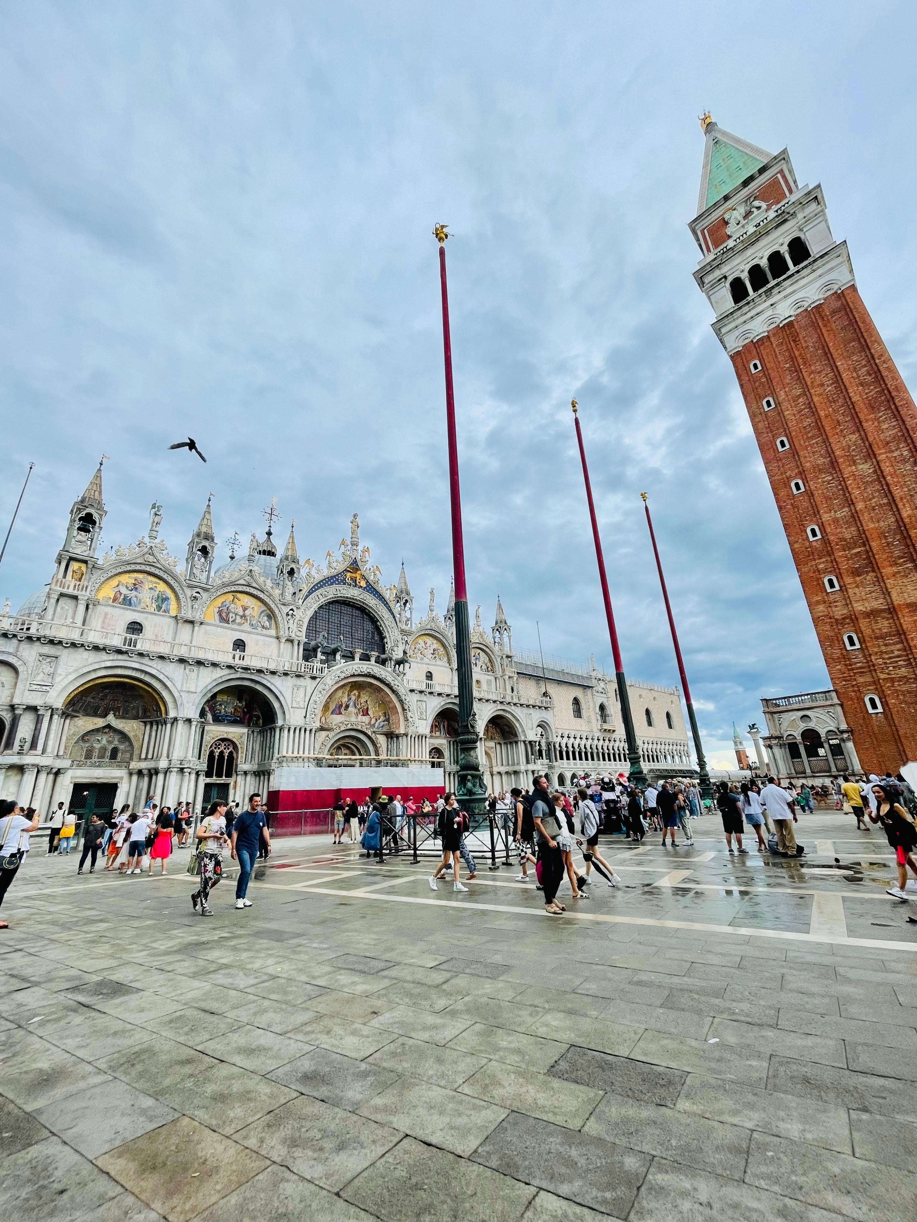 View of a city plaza with clock tower and pedestrians walking on a cloudy day