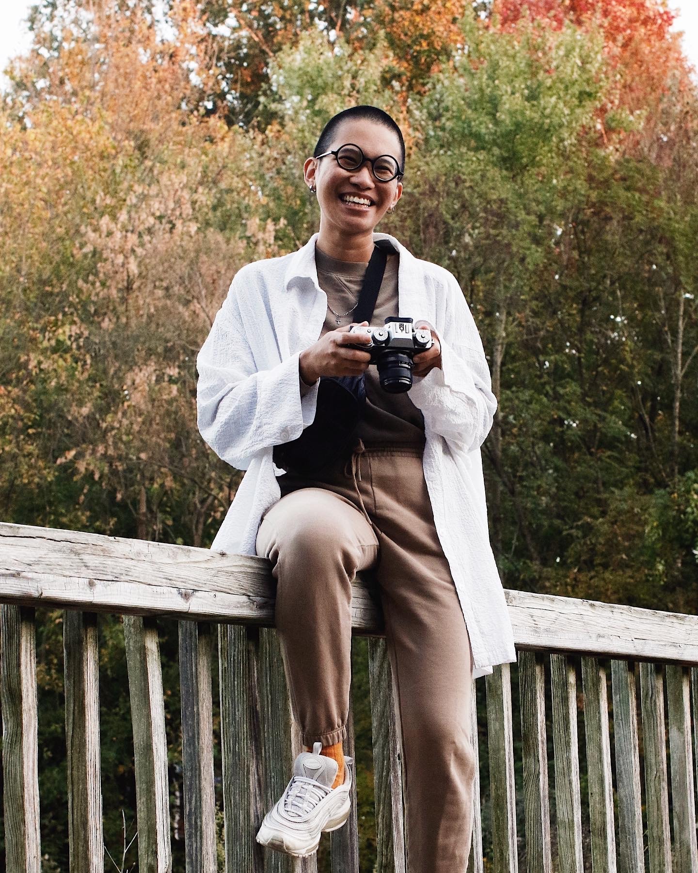 Advisor in a white jacket sitting on a wooden fence with trees in the background