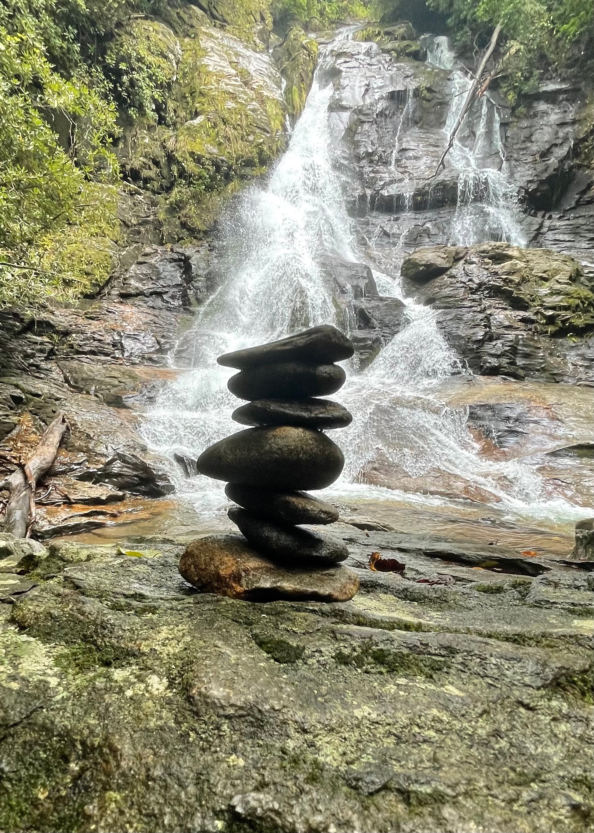 A picturesque view of carefully balanced rocks positioned before a flowing waterfall