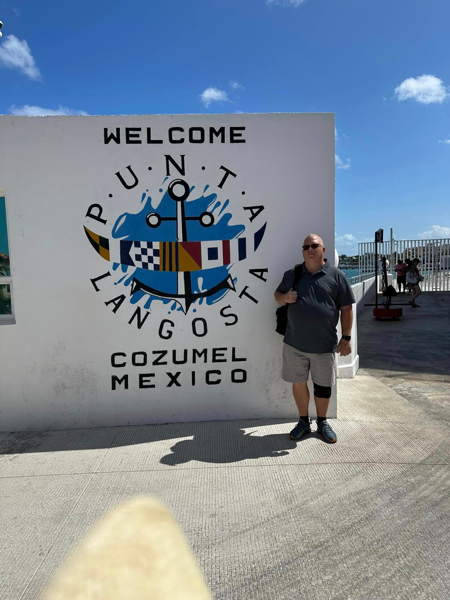 Advisor standing by a wall with a welcome to Cozumel, Mexico under sunny skies