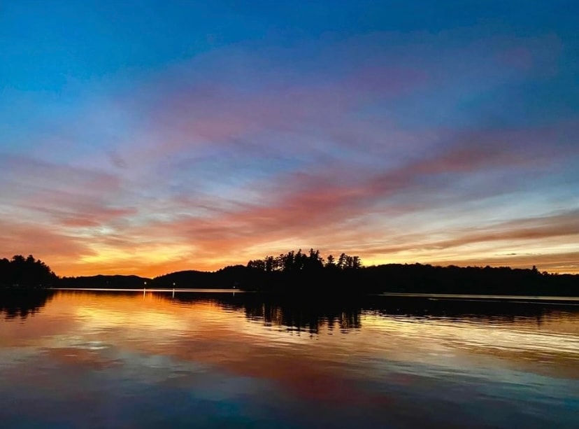 View of a beautiful sunset over a glassy lake lined with trees