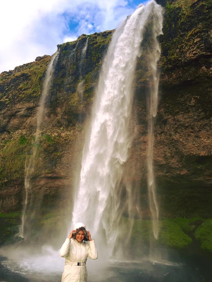 Advisor in a white jacket at the base of a tall waterfall on a sunny day