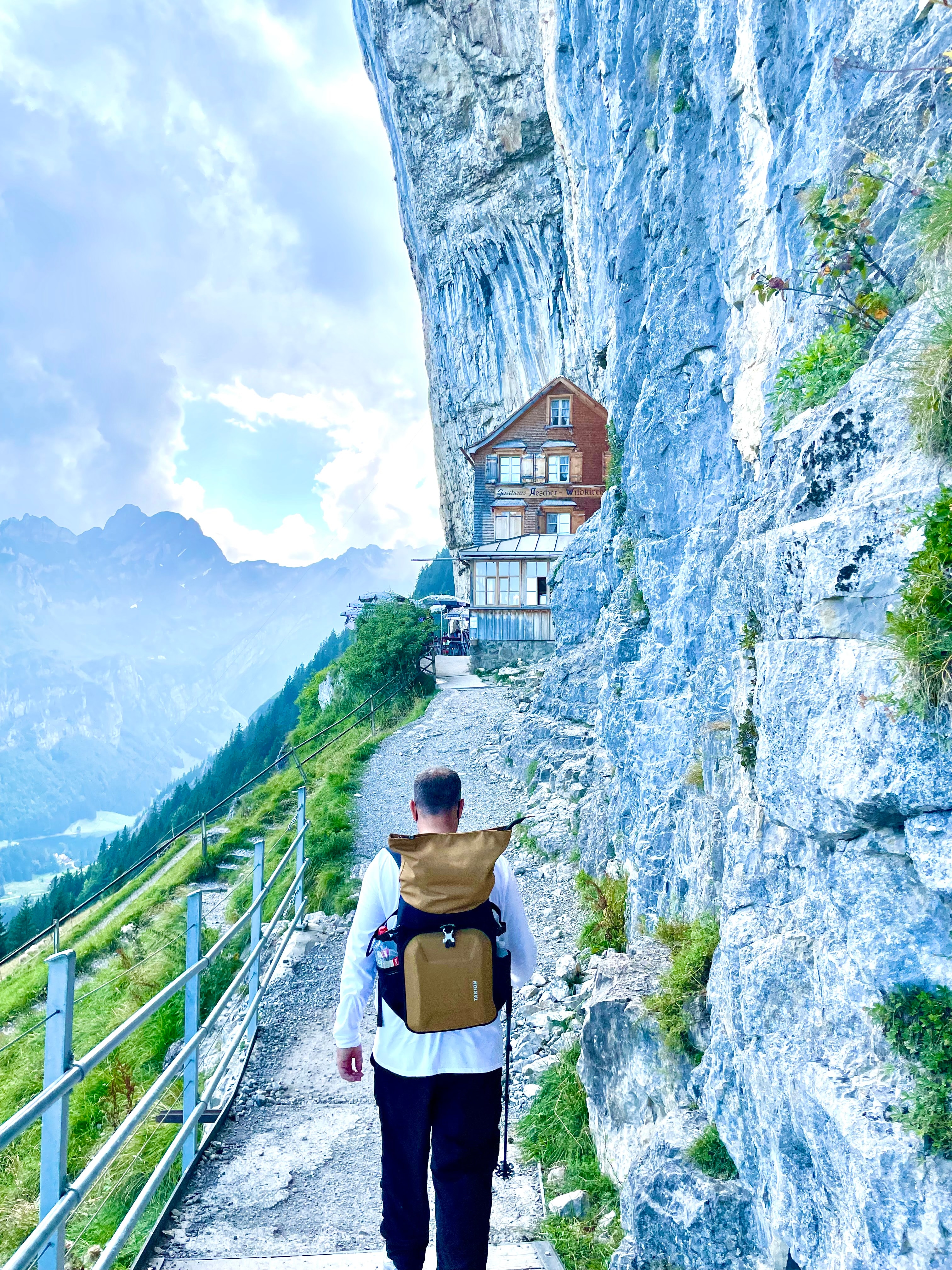 Advisor hiking along a mountain pathway with dramatic cliffs to one side on a cloudy day