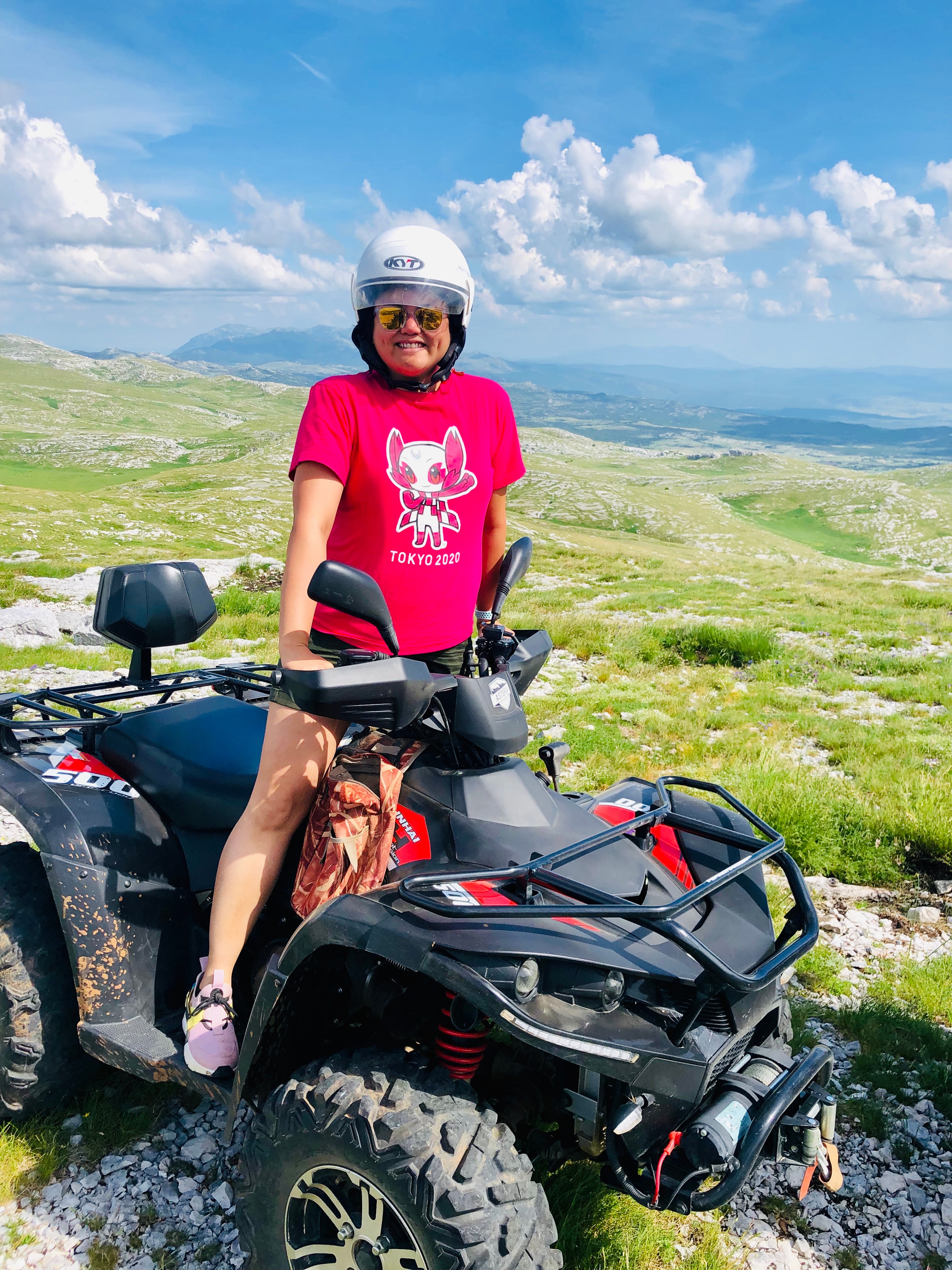 Advisor wearing a white helmet and standing on a black ATV in the mountains on a sunny day