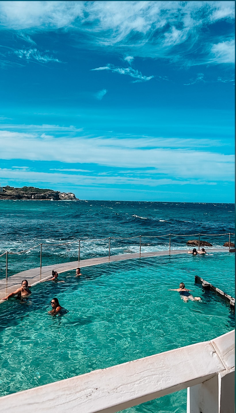 View of an infinity pool with several people swimming overlooking the sea on a sunny day