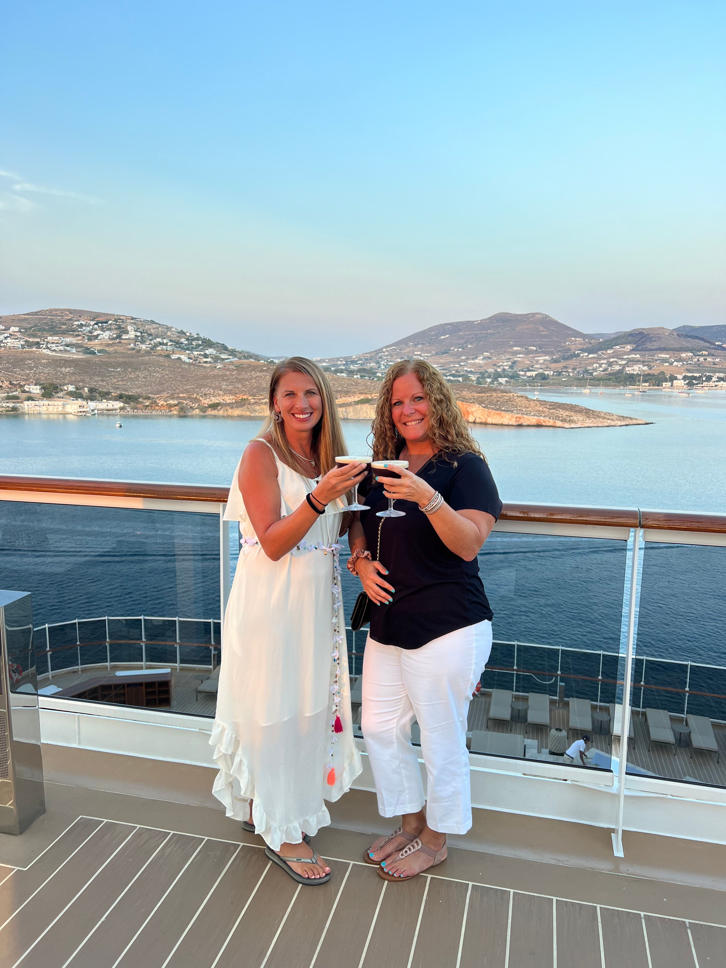 Advisor and friend holding cocktails on the deck of a boat with an island coastline behind them