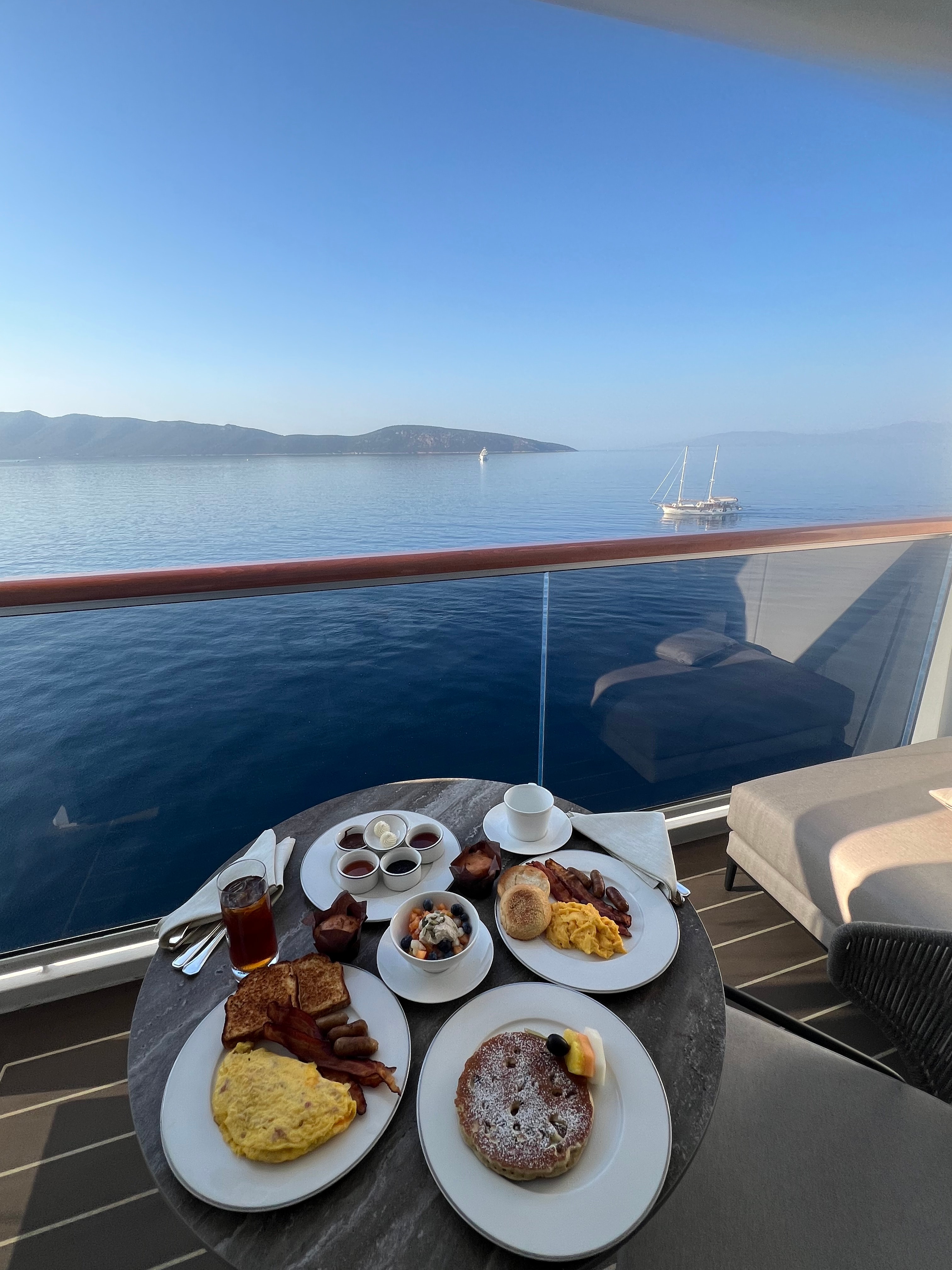 Plates of breakfast food set on a small circular table on a balcony overlooking the sea