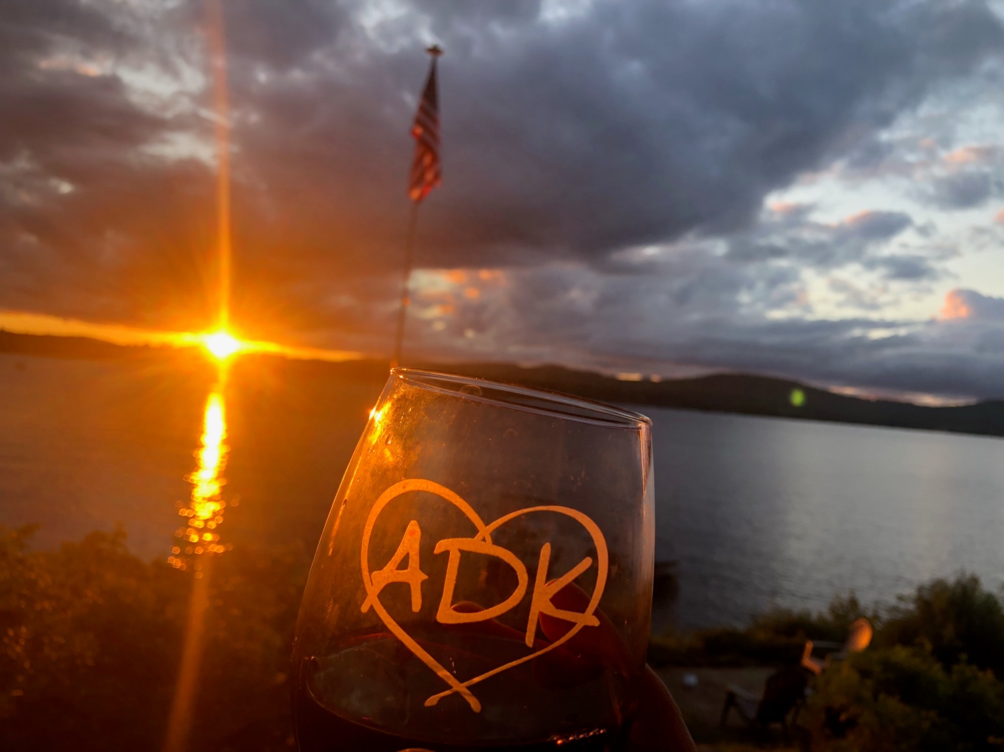 View of a wine glass with initials ADK in a heart and an orange sunset over the sea behind it