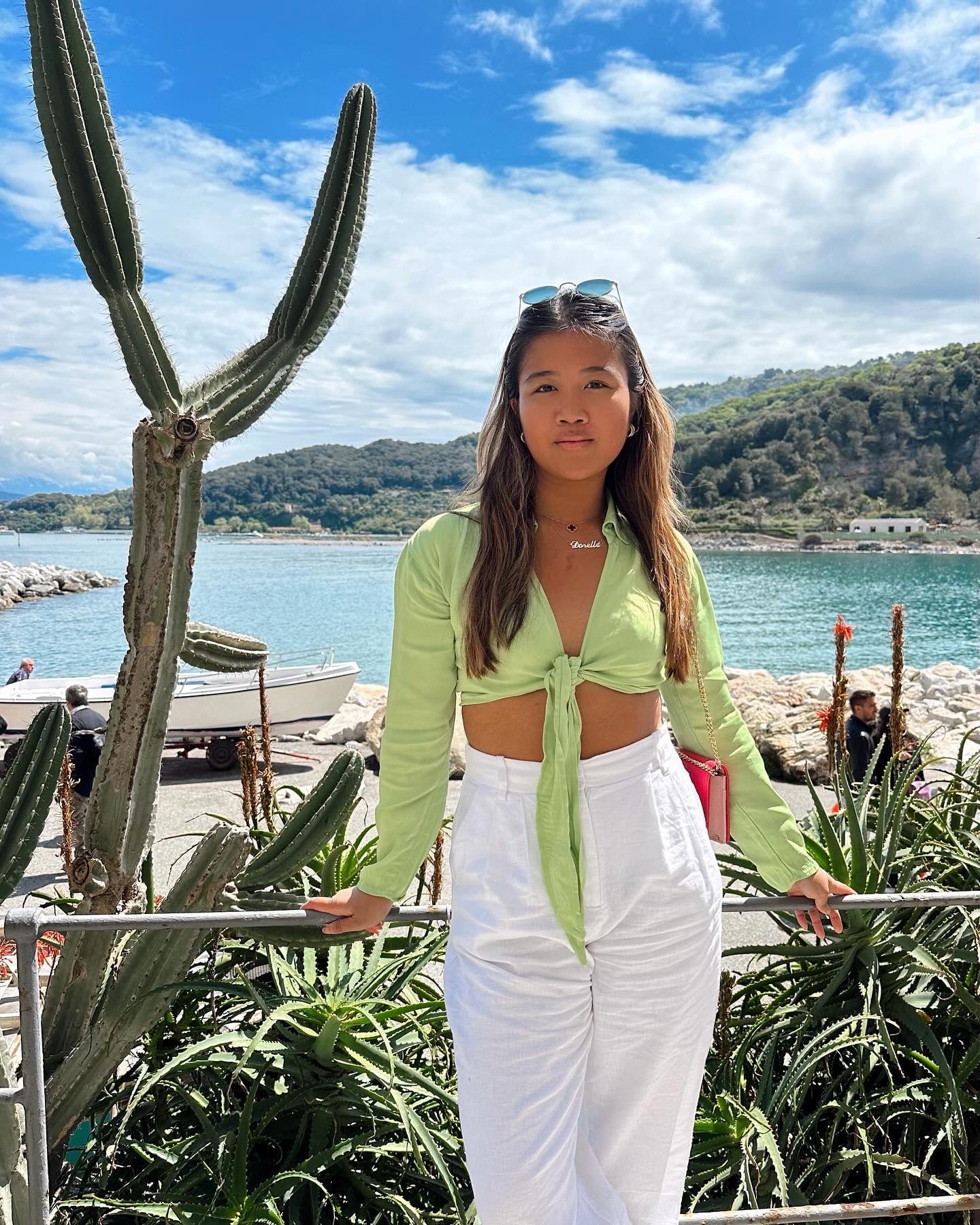 Advisor in white pants and a green top posing by plants on the beach in Italy