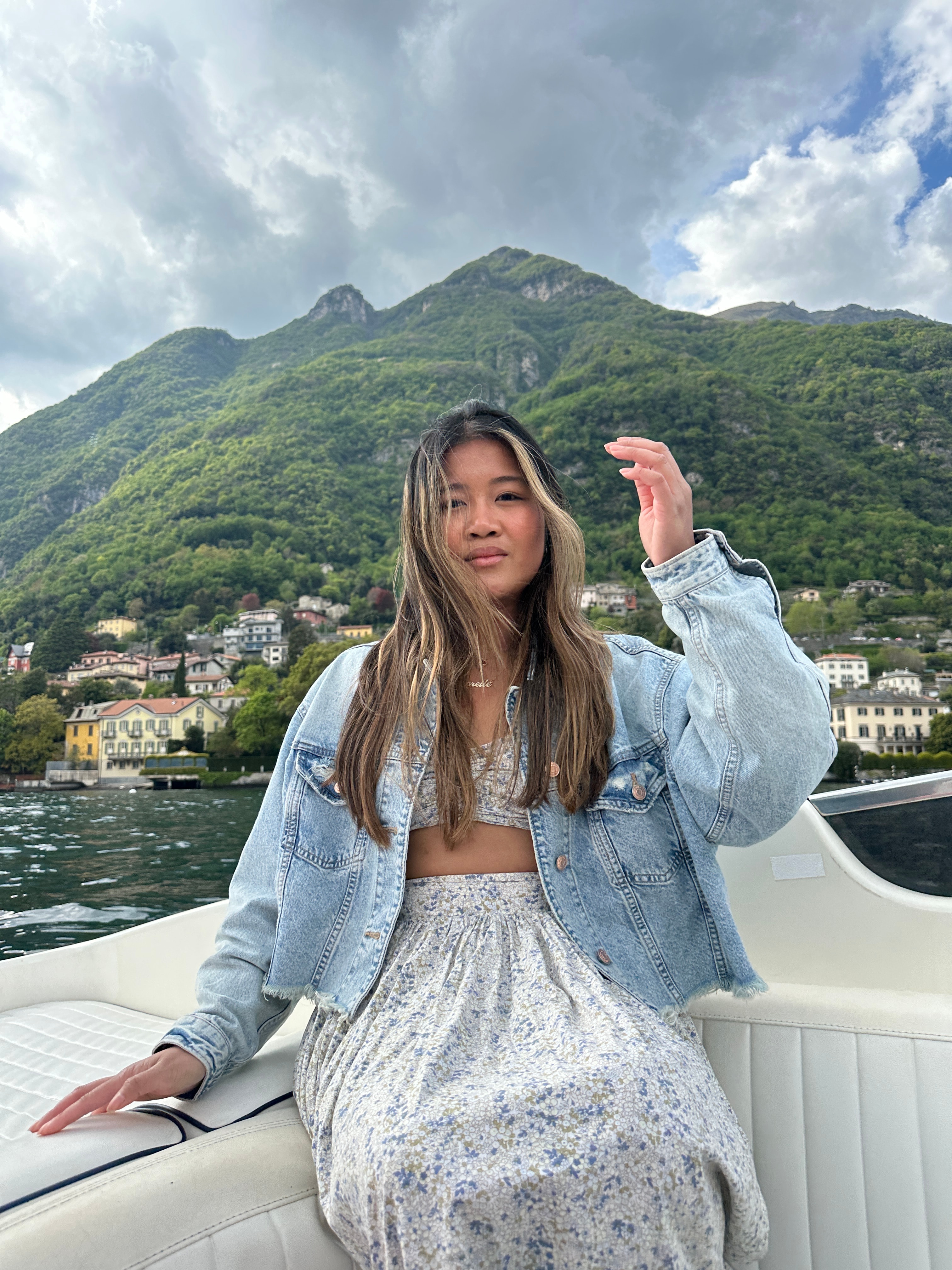 Advisor wearing a denim jacket and sitting on the back of a boat on a lake with a green mountain rising in the background