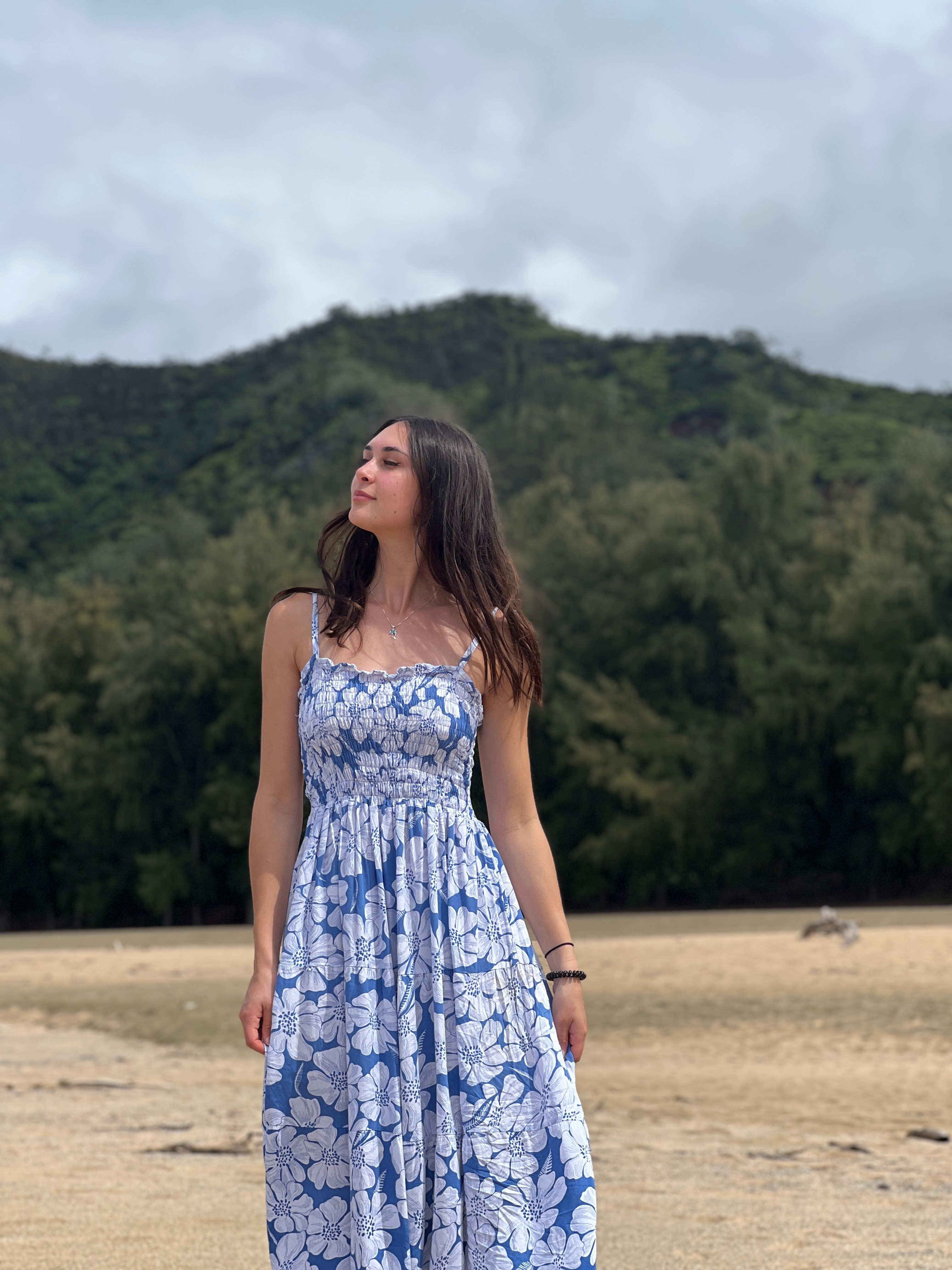 Advisor in a long blue and white dress posing on an empty beach lined with trees on a cloudy day