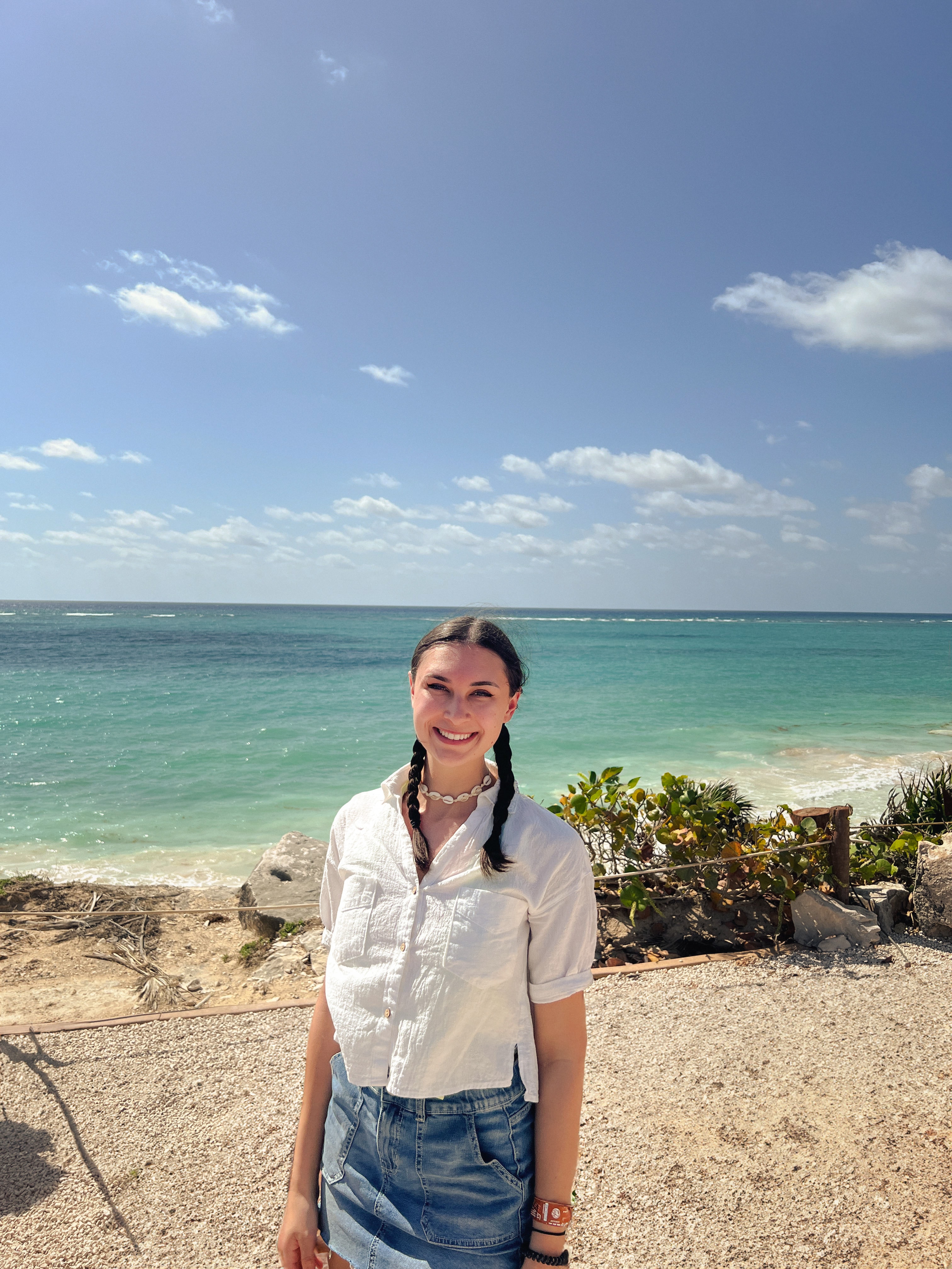 Advisor in a white shirt and denim skirt smiling on the beach with a calm sea behind her