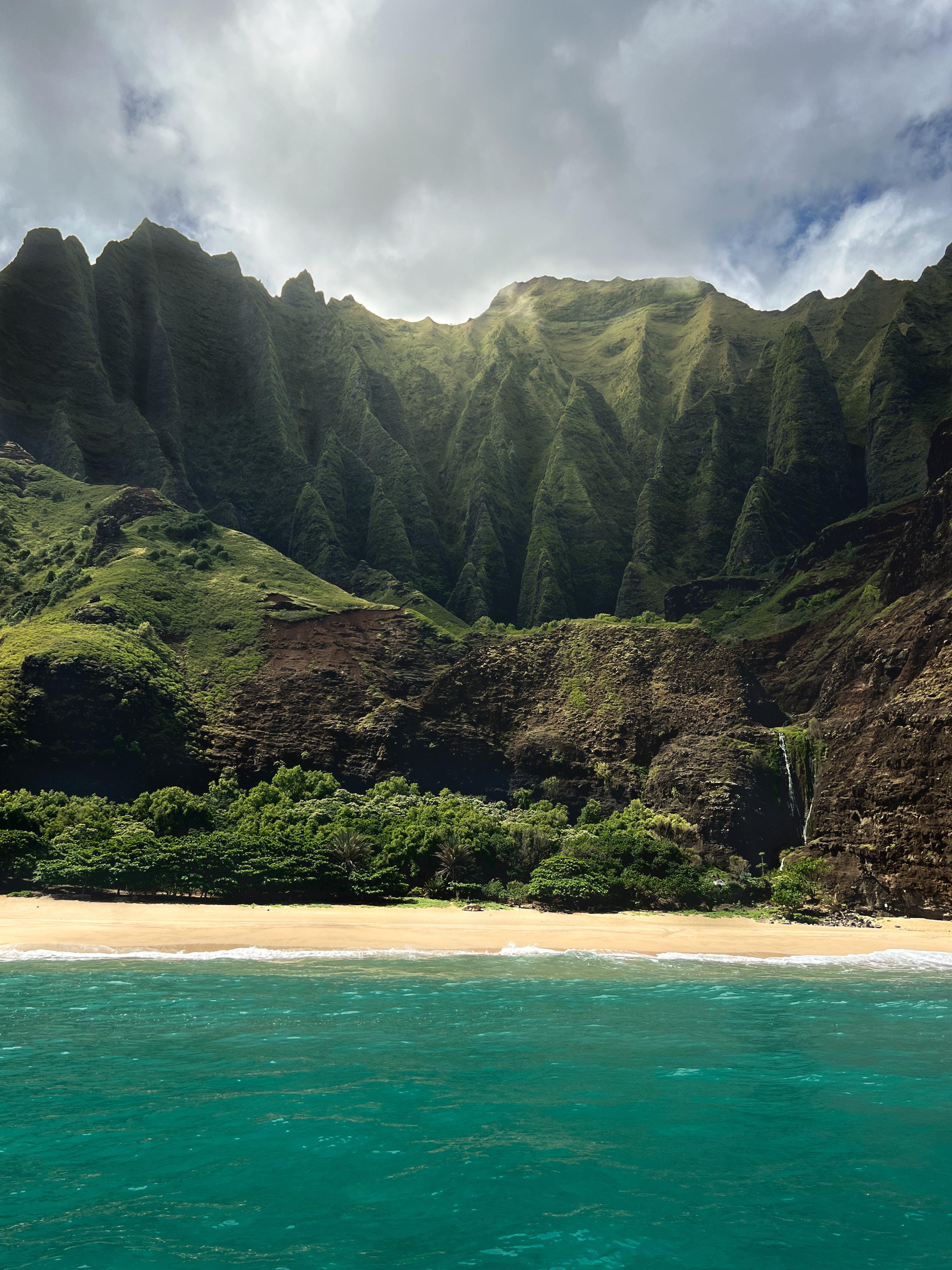 View of a beautiful empty white sand beach with lush mountains rising above on a sunny day