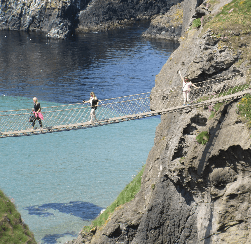 Overhead view of three people walking along a rope suspension bridge over the sea