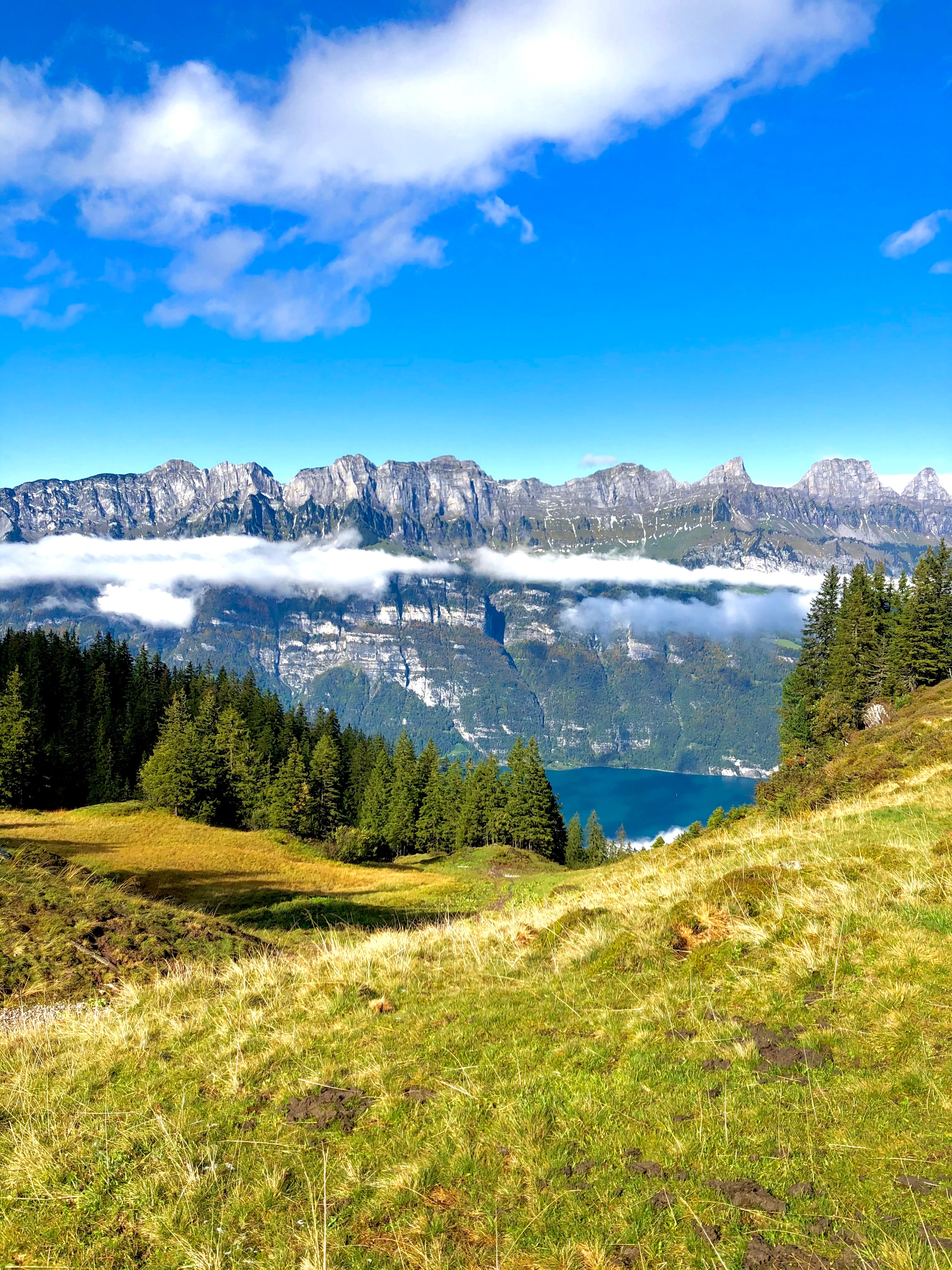 Stunning view of a glassy lake reflecting a snowy mountain landscape and green hills on a sunny day