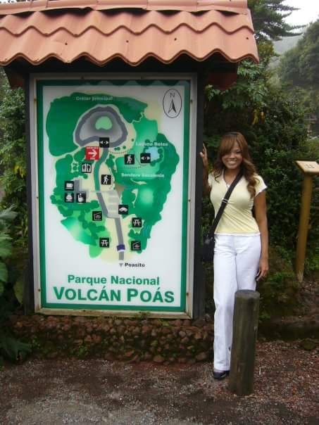 Advisor smiling beside a sign for Volcan Poas on a cloudy day