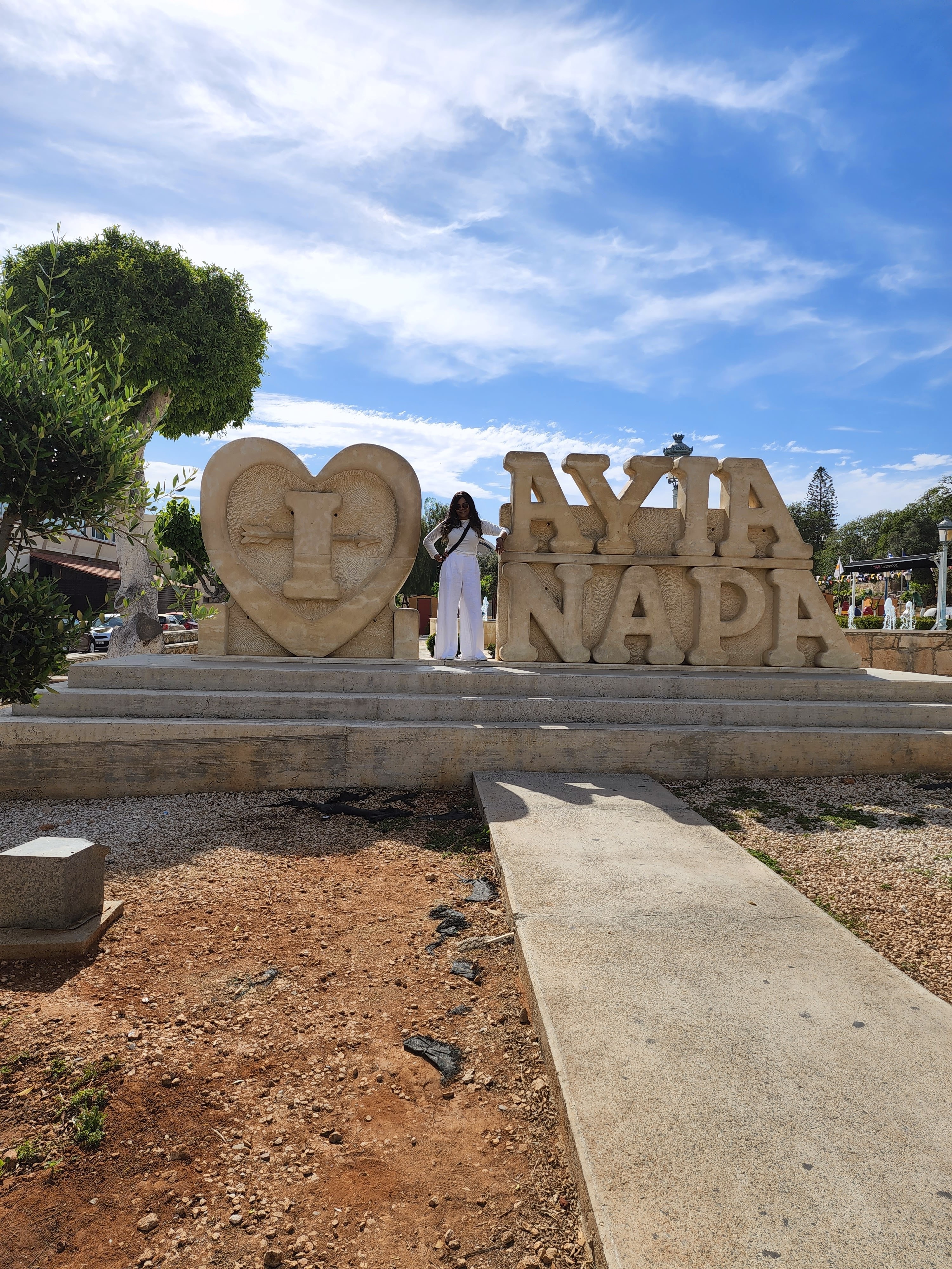 Advisor posing on a stone sign with a heart and “AYIA NAPA” in carved lettering on either side