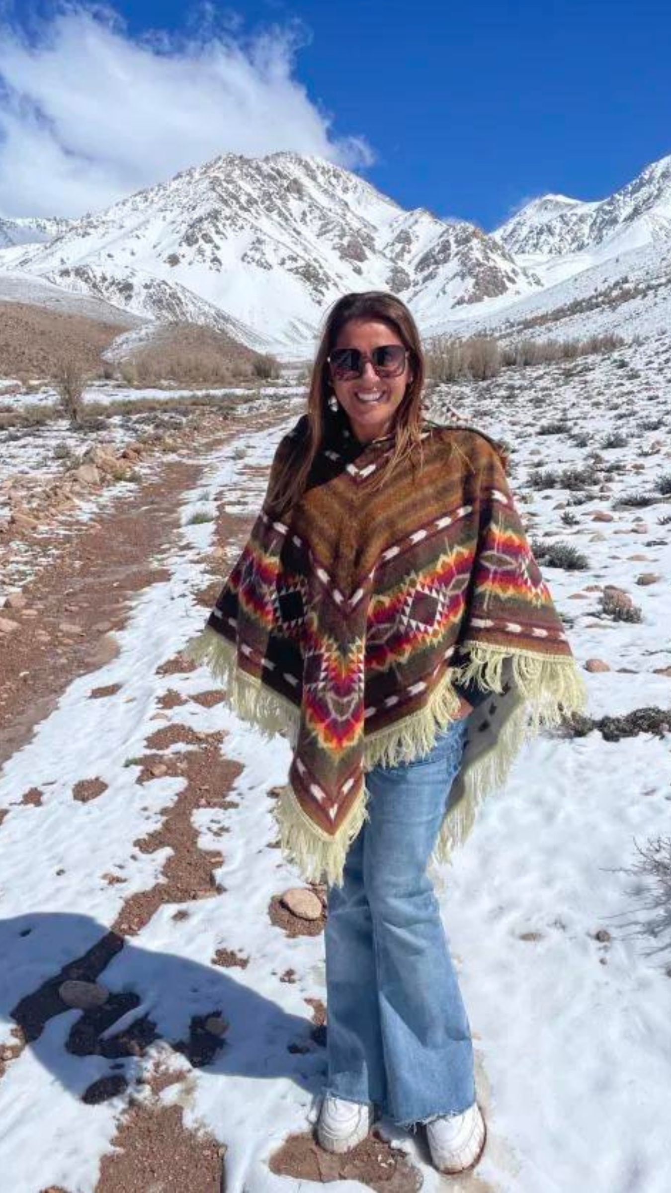 Advisor in a knit shawl smiling in a snowy environment with mountains in the distance on a clear day