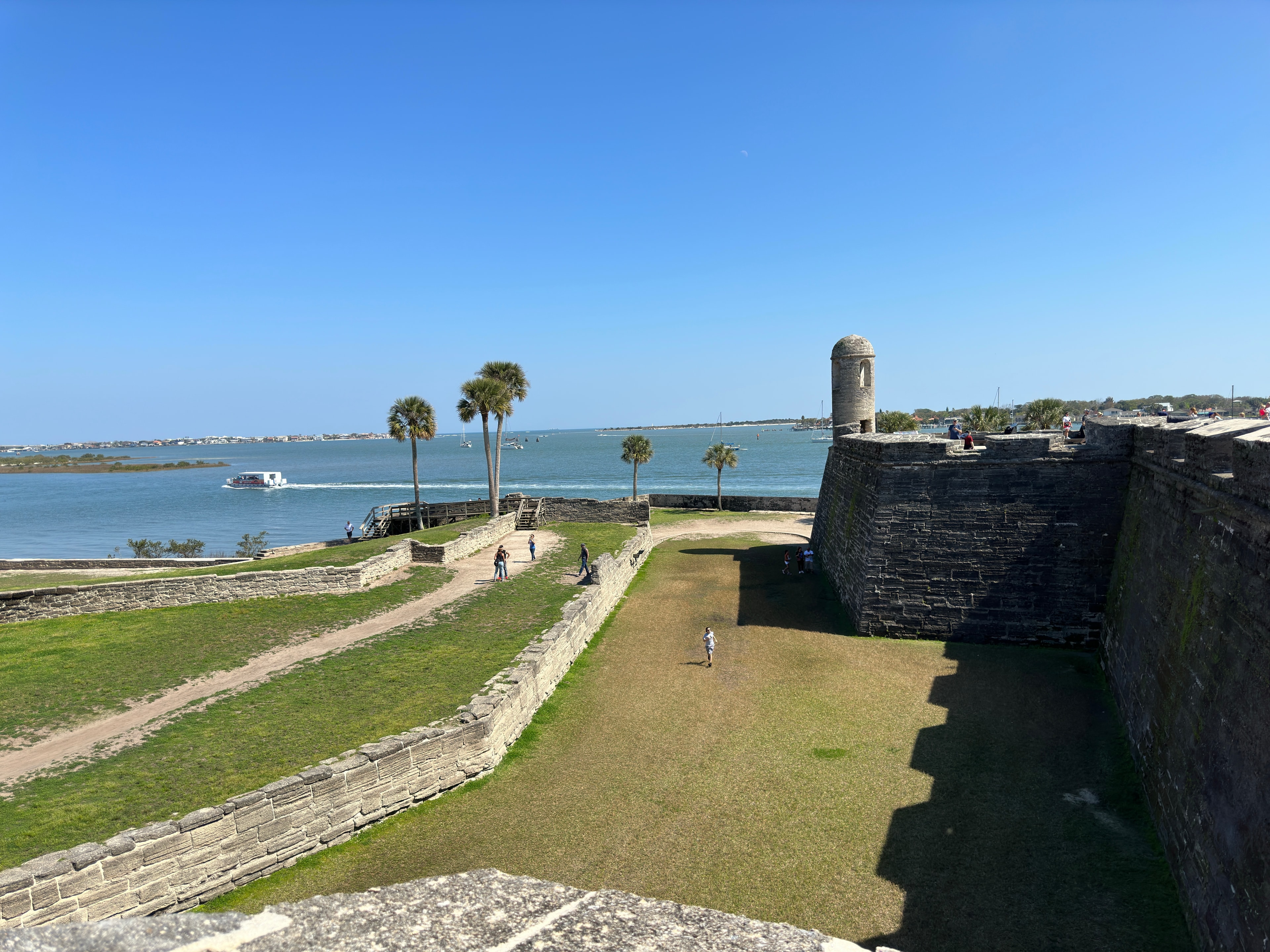 A view of the ocean with palm trees in the distance on a sunny day. 