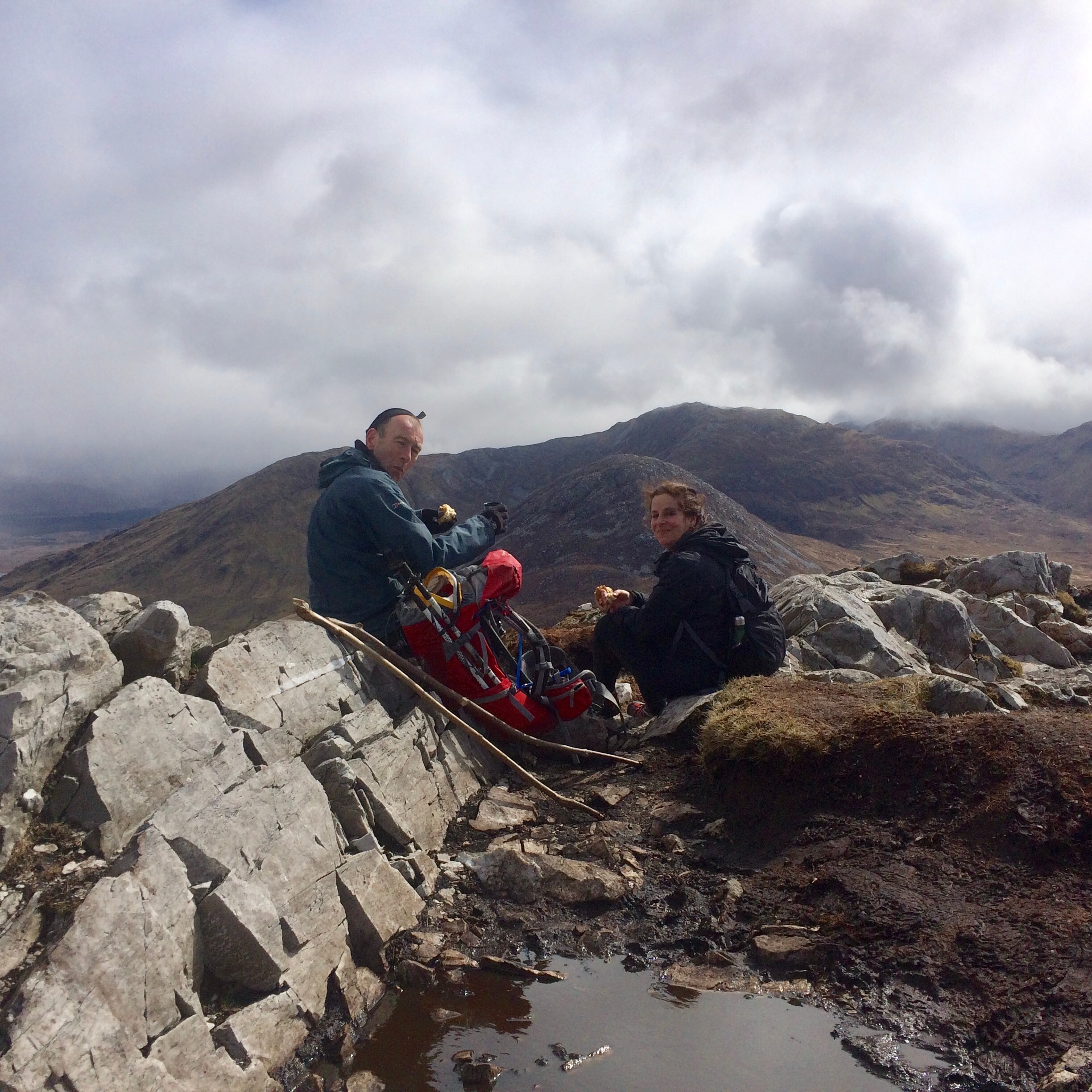 Advisor and partner sitting on rocks atop a cloudy mountain while on a hike