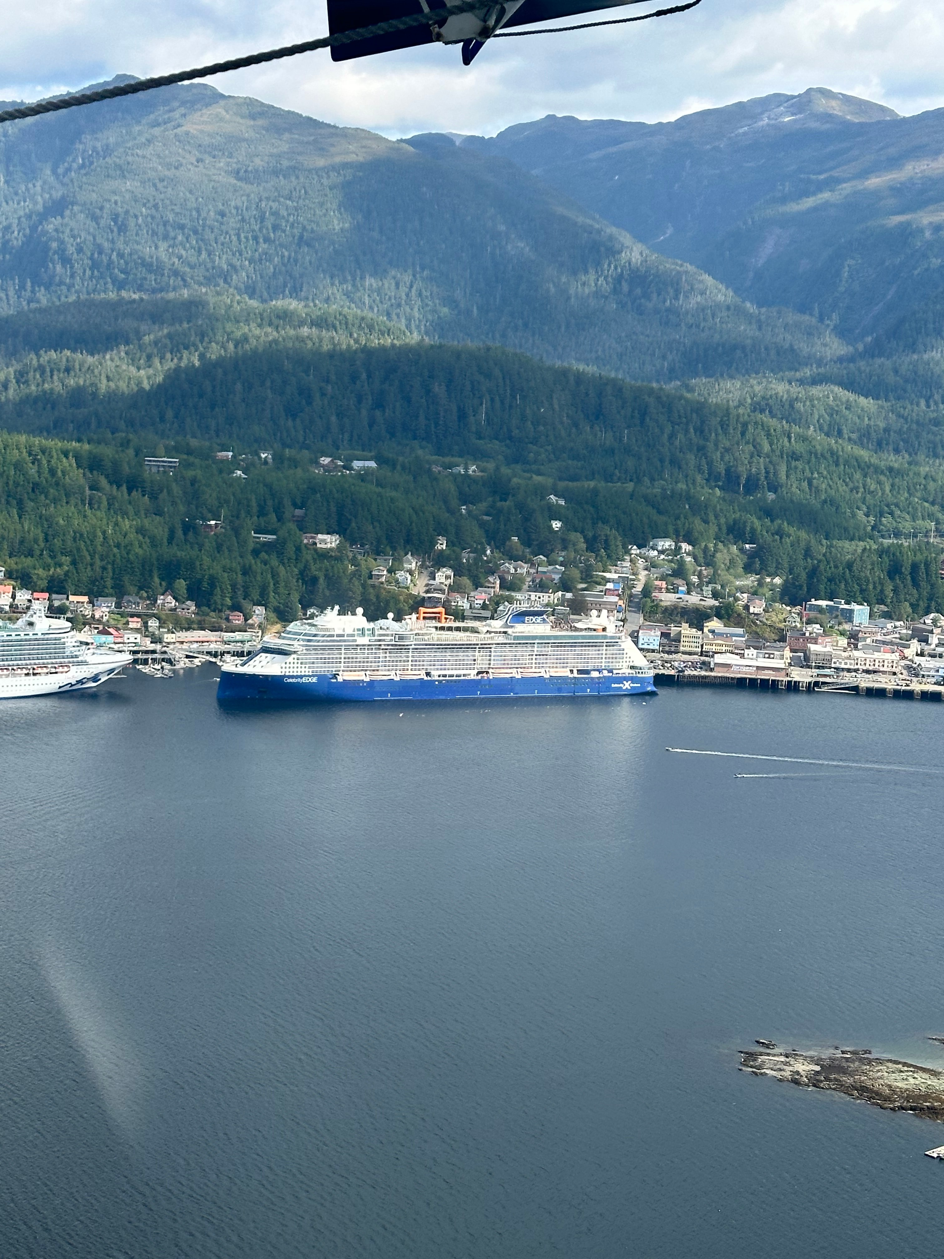 View of a cruise ship leaving port with rolling green hills and coastal town behind it