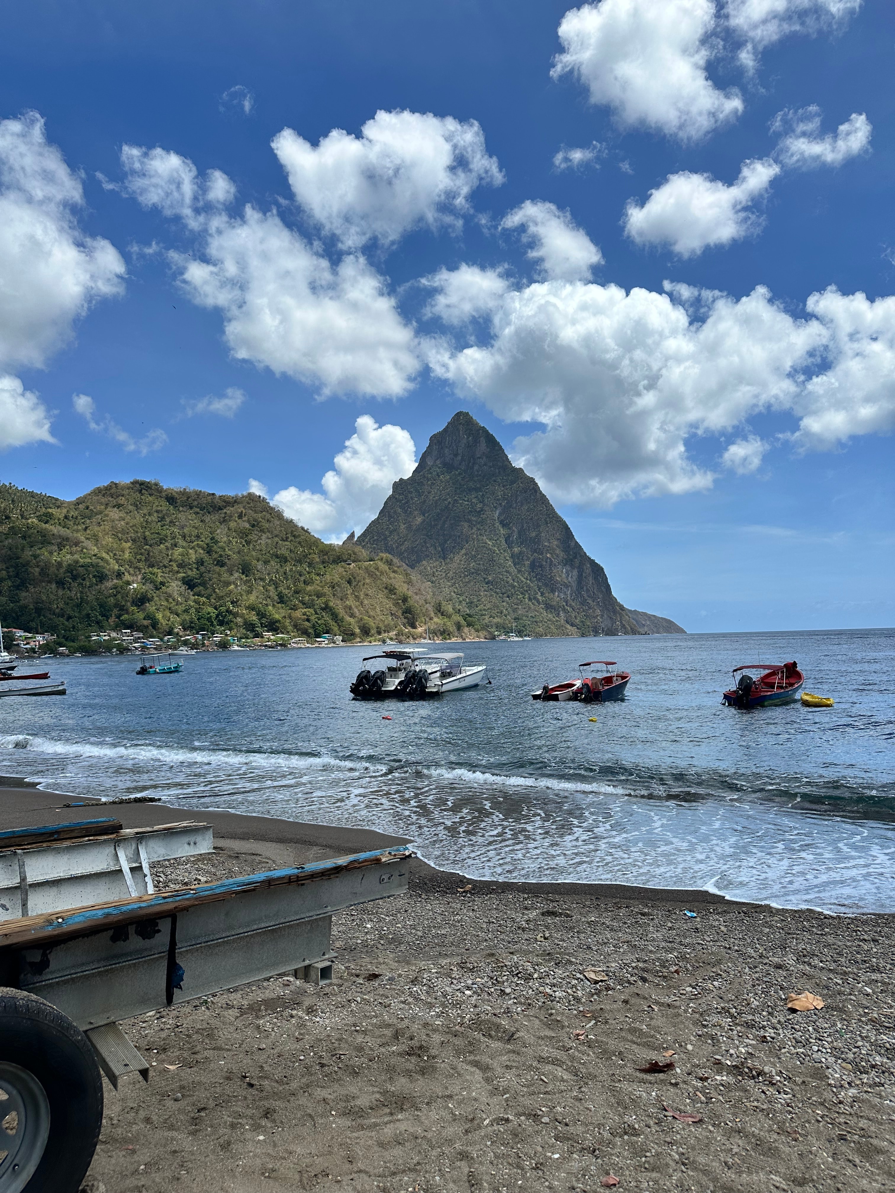 View of lush green mountains as seen from a beach with small boats anchored offshore