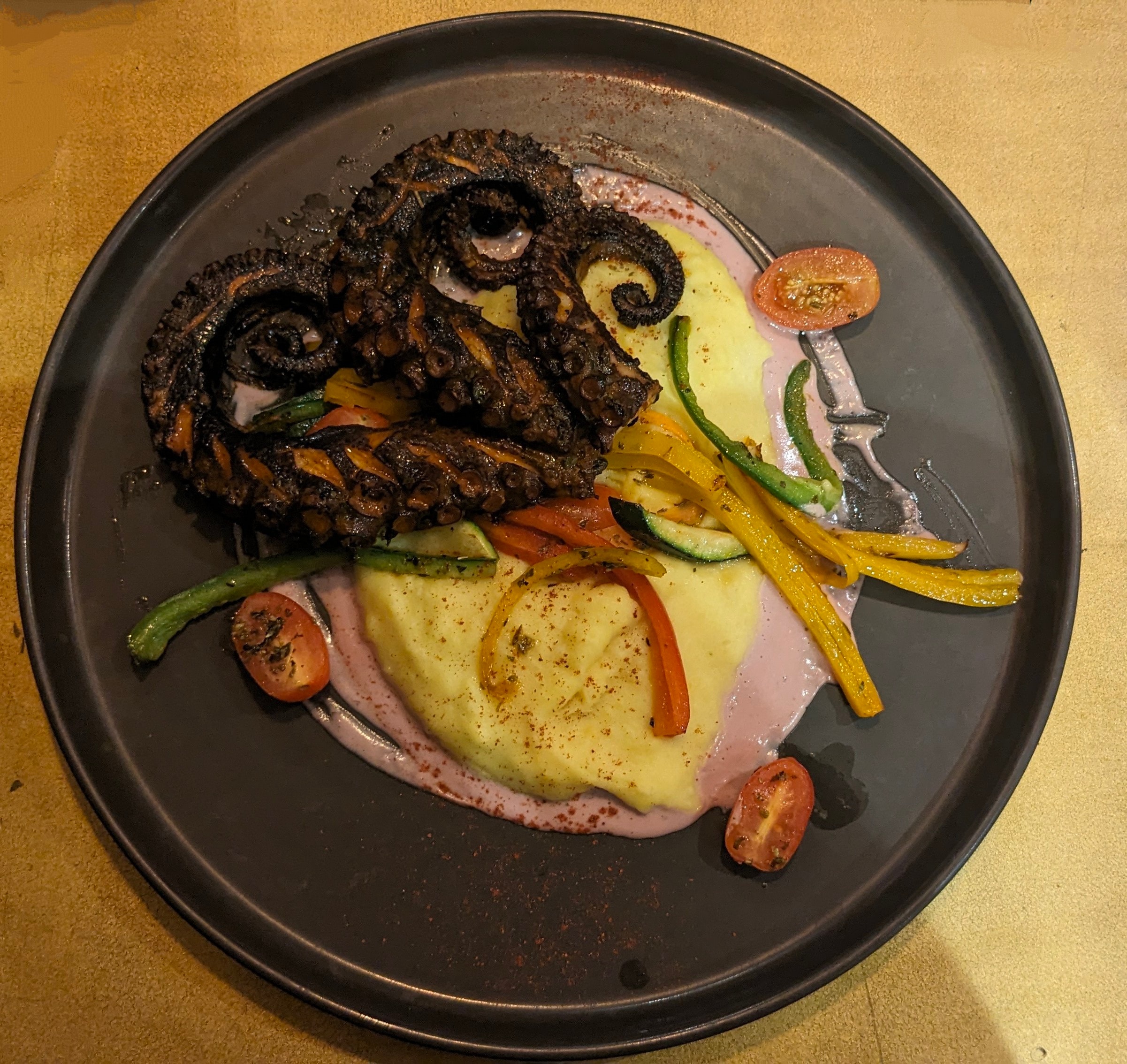 View of a black plate with grilled octopus and mashed potatoes