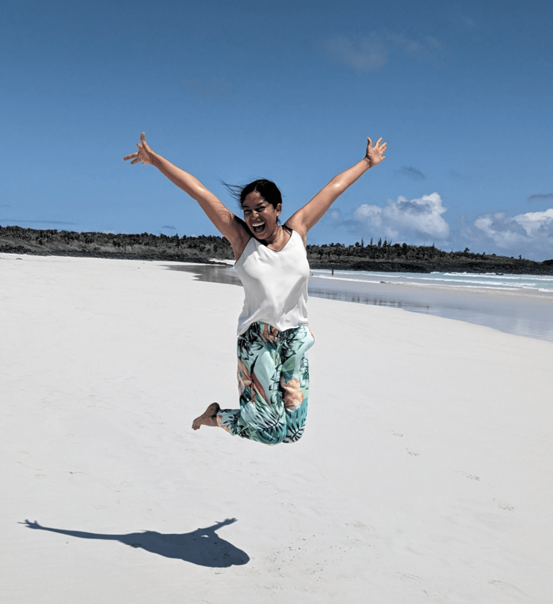 Advisor jumping on a pristine white sand beach in the Galapagos with arms raised in the air