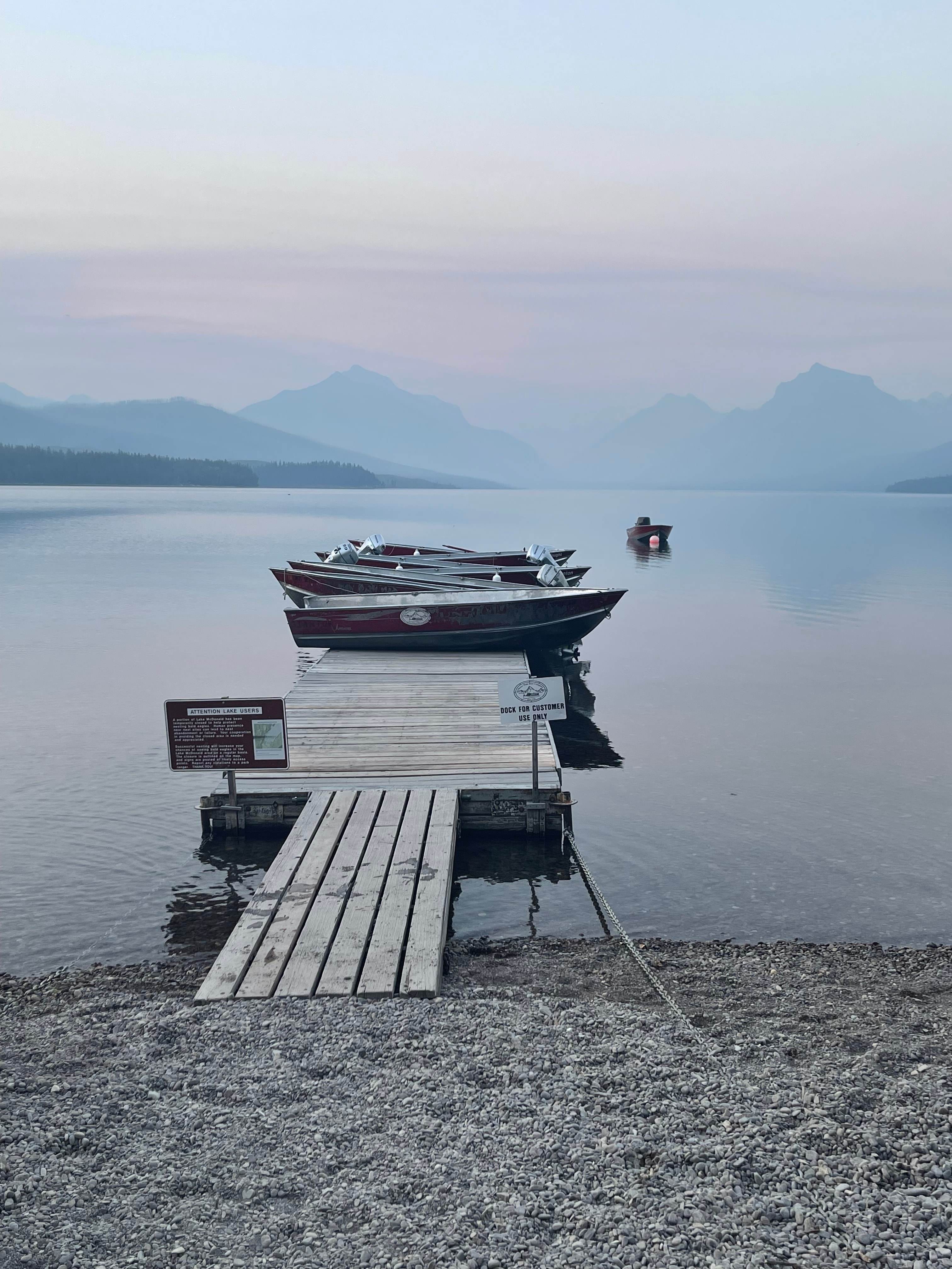 View of a short wooden pier with small fishing boats anchored at its end at dusk