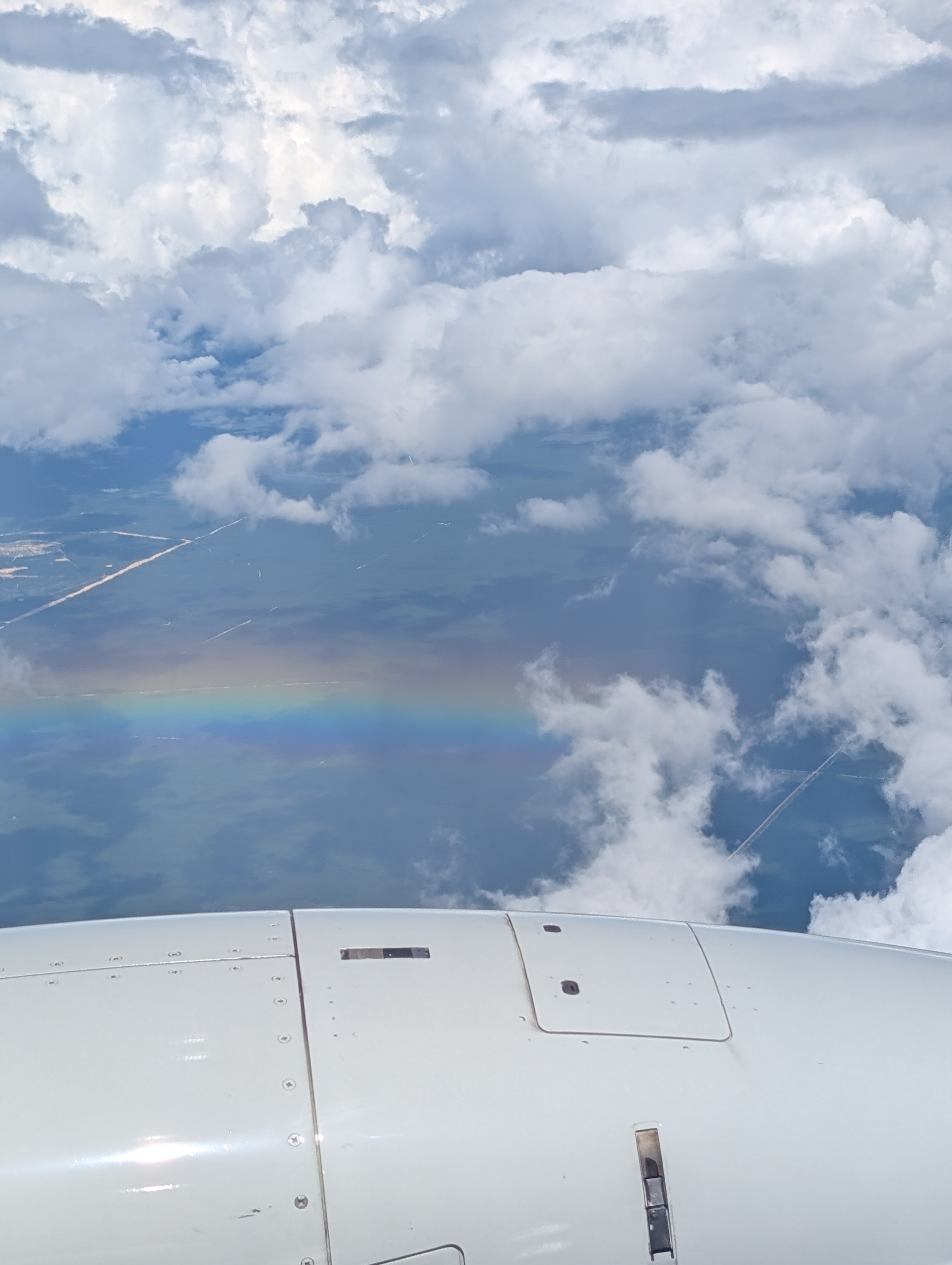 View of a rainbow and white clouds as seen from high above through a plane window