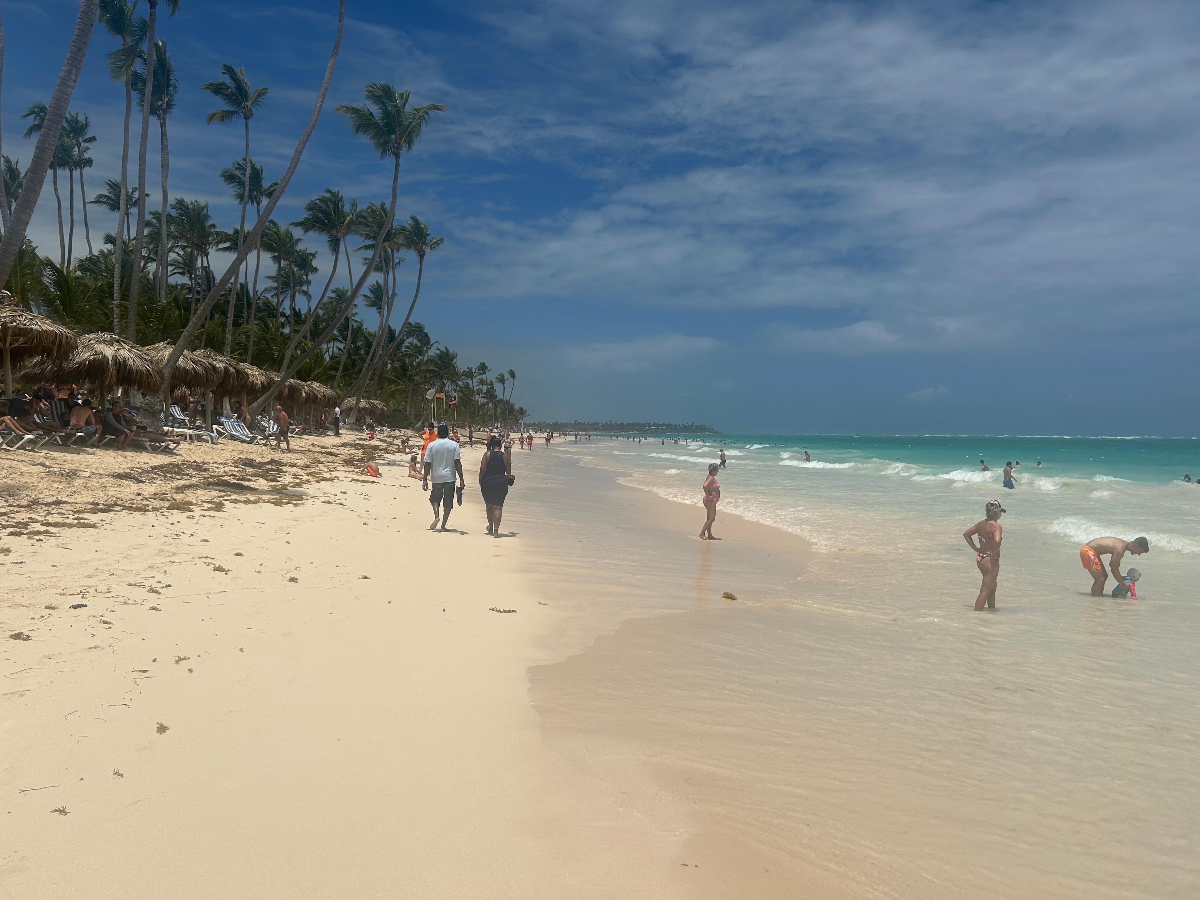 Wide white sand beach with a few people walking and standing in shallow water on a sunny day