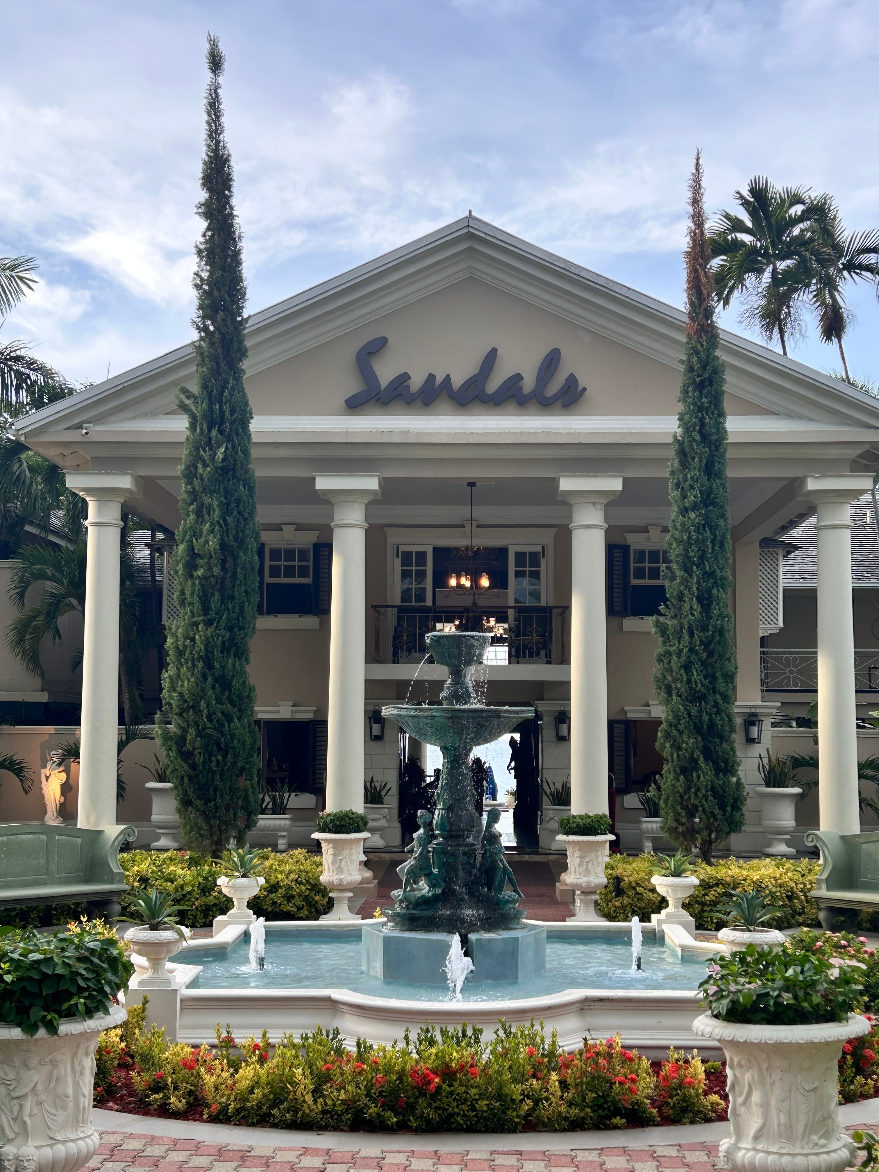 View of the facade of a Sandals property with a fountain and statue in front