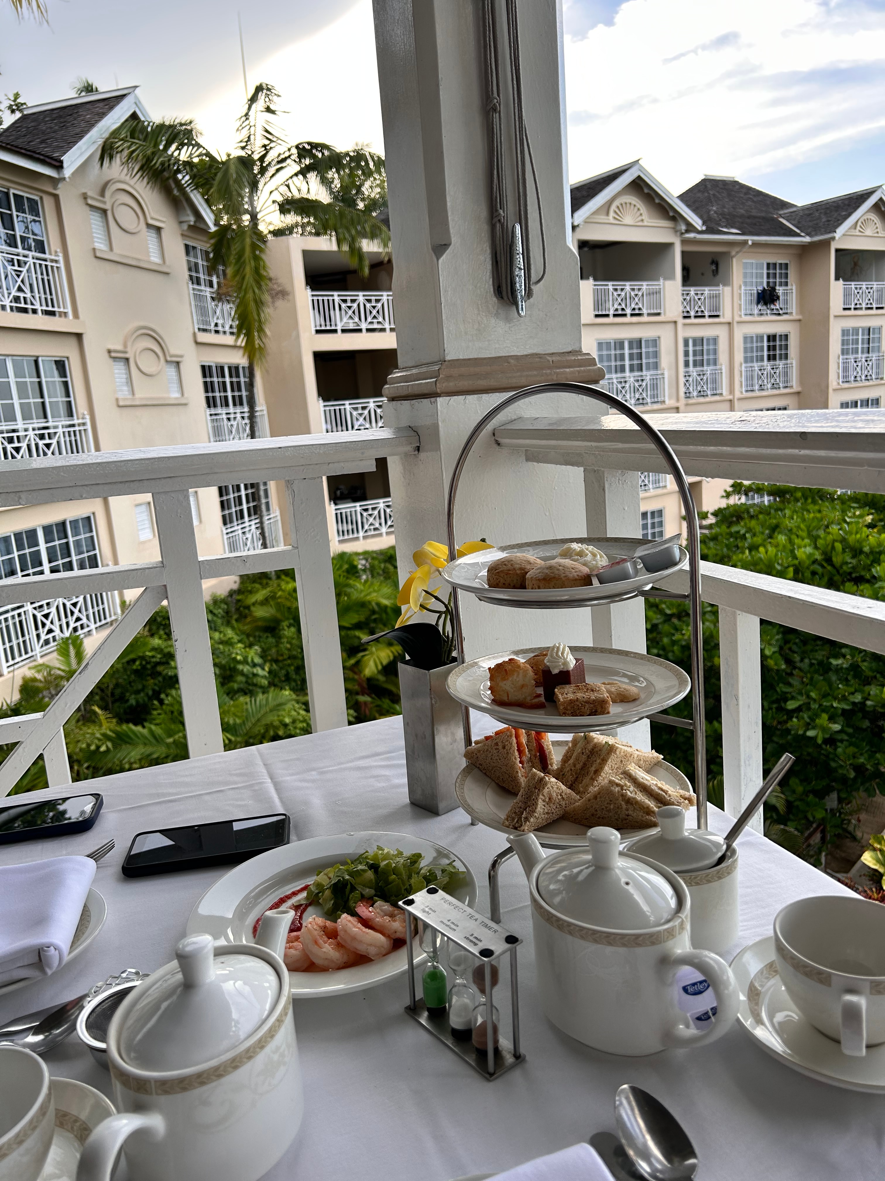 View of a three-tiered tray of scones and mini sandwiches on a table on a balcony overlooking resort accommodation