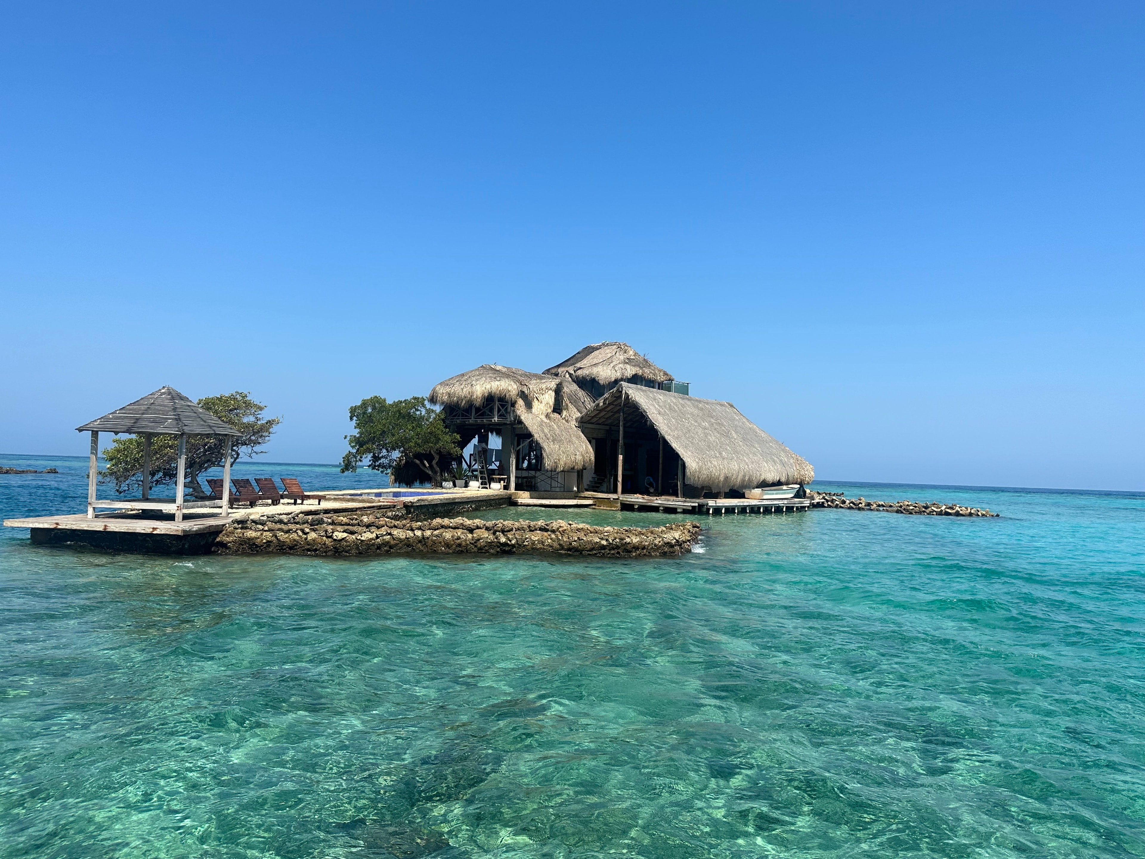 View of a thatched-roof structure over crystal clear ocean water on a sunny day