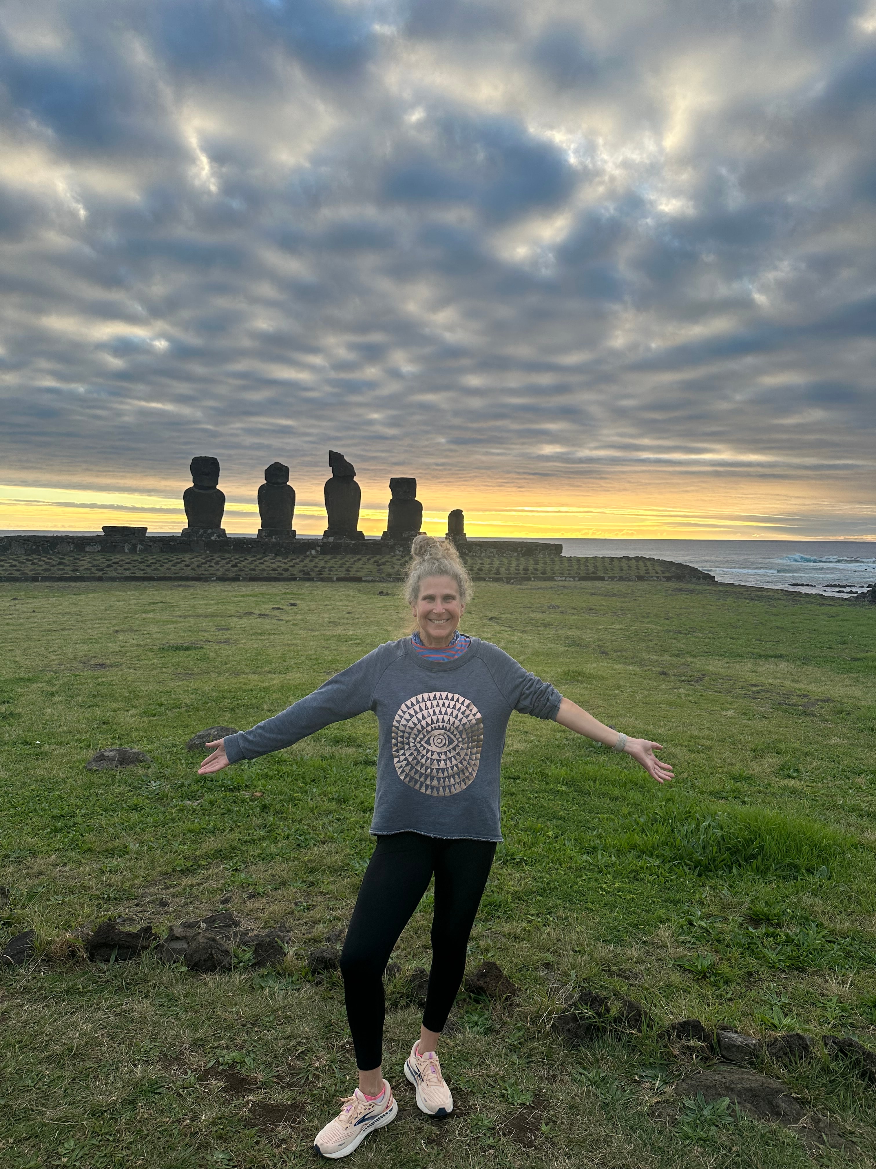 Advisor standing with arms outstretched on a grassy field at sunset with stone towers in the distance behind her