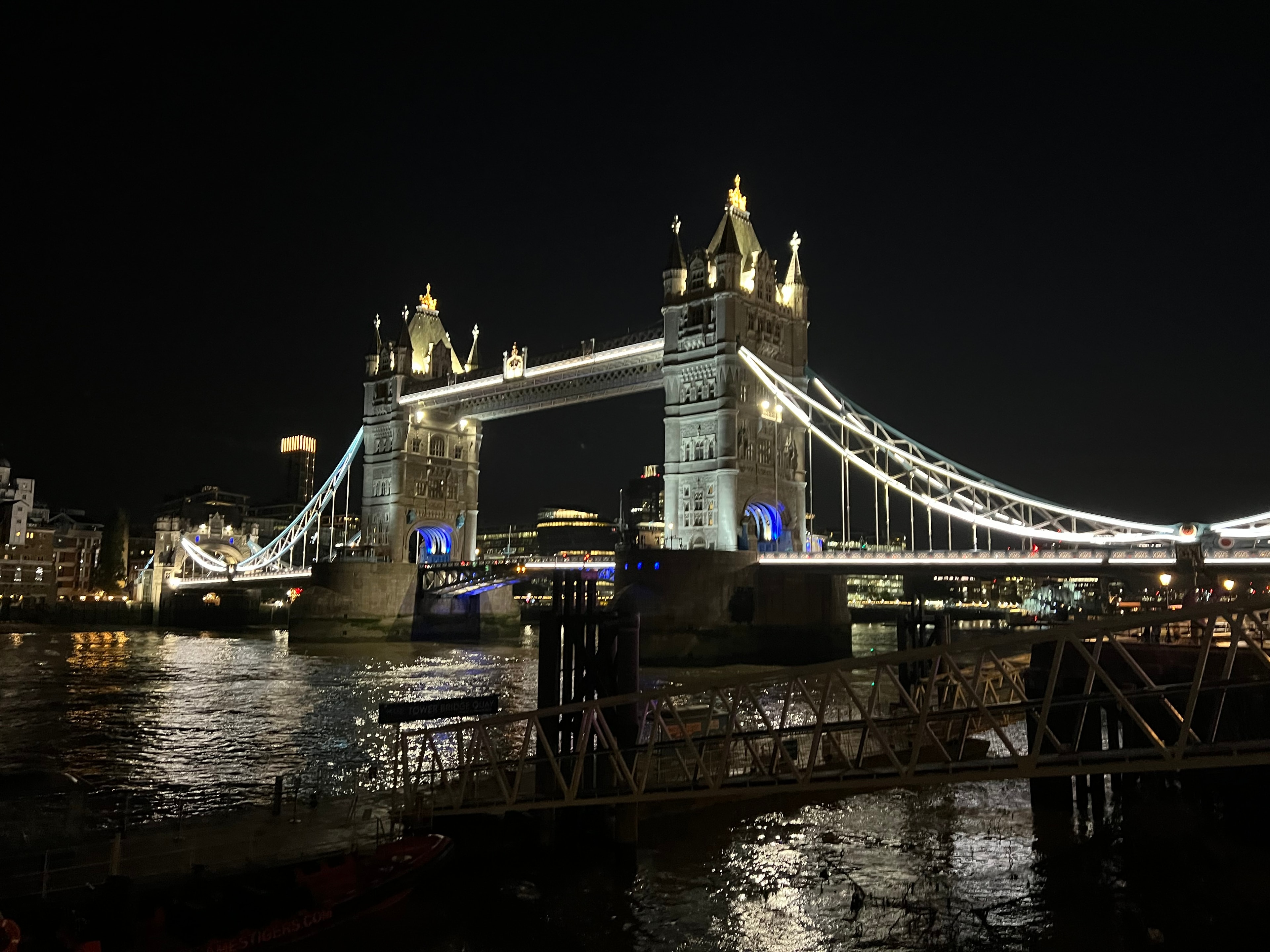 Photo of a bridge lit up at night with water underneath.