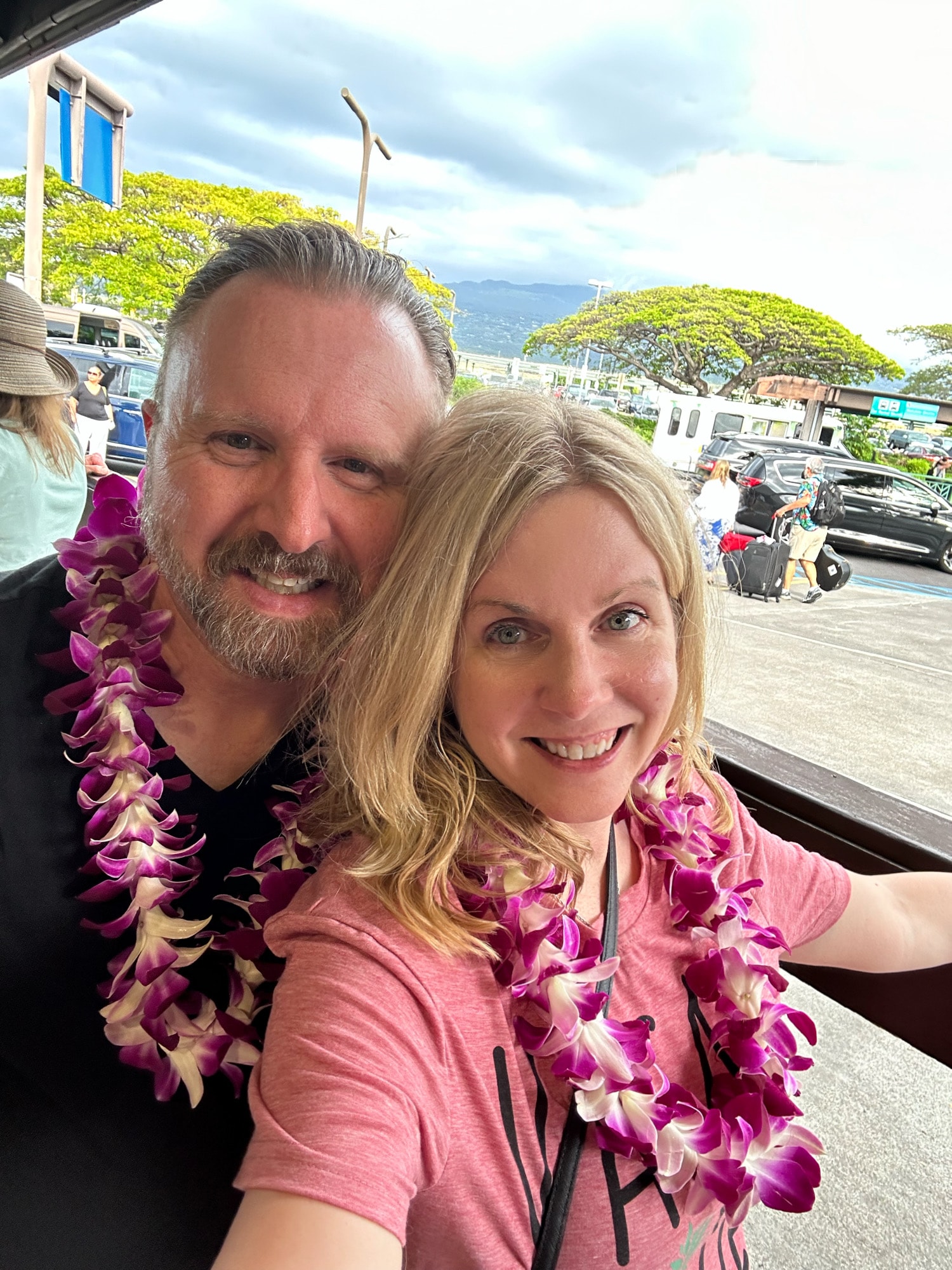 Advisor and partner both wearing pink leis and taking a selfie outdoors