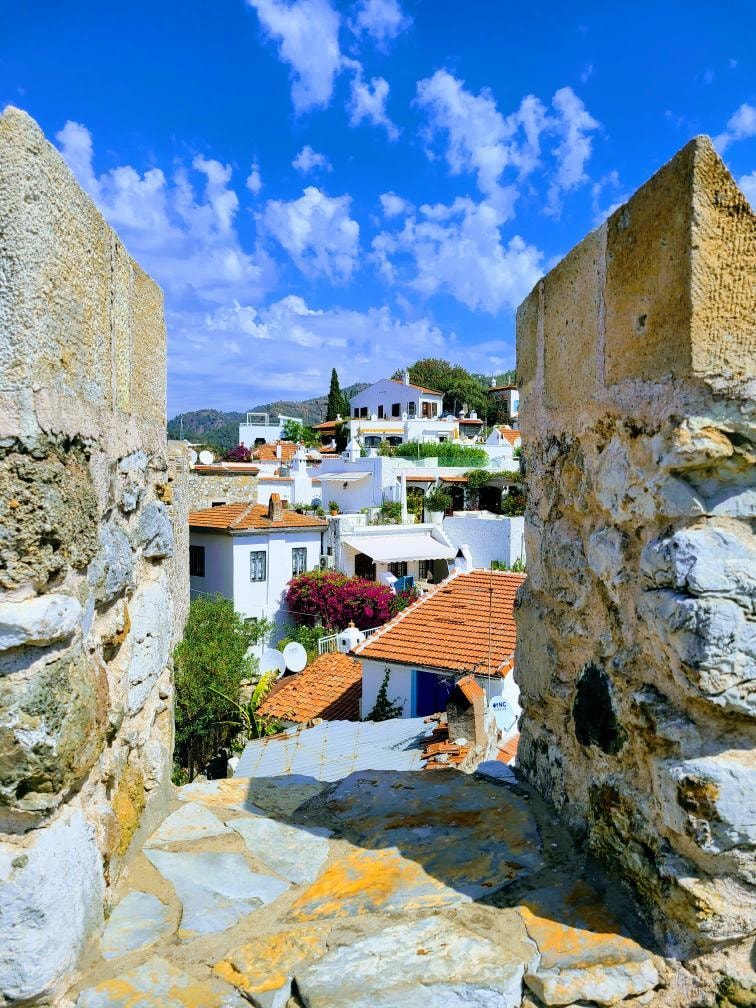 View of white buildings with orange-tiled rooftops on a sunny day as seen from the opening of a stone structure