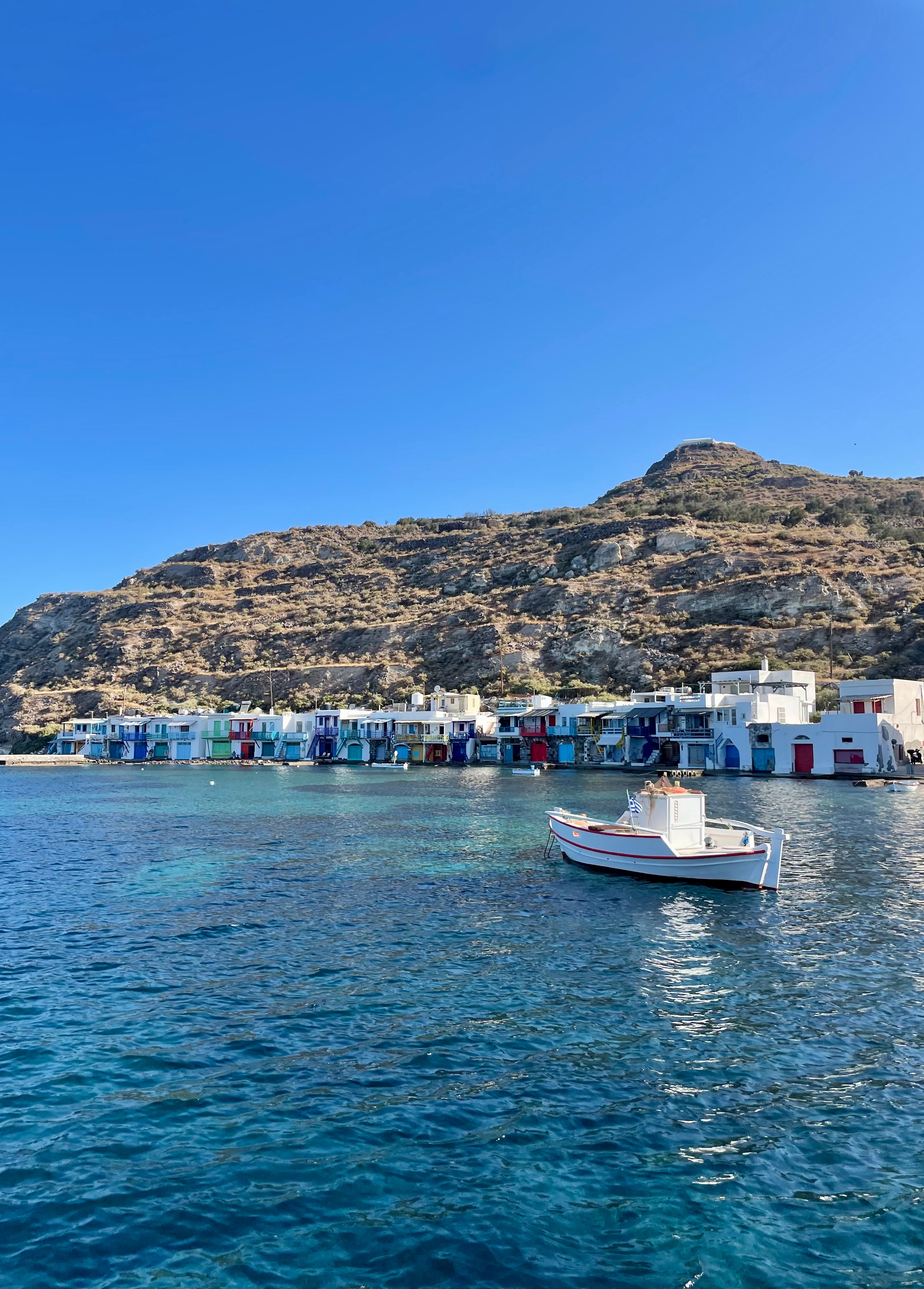 View of a singular white boat sailing towards a coastline under clear skies