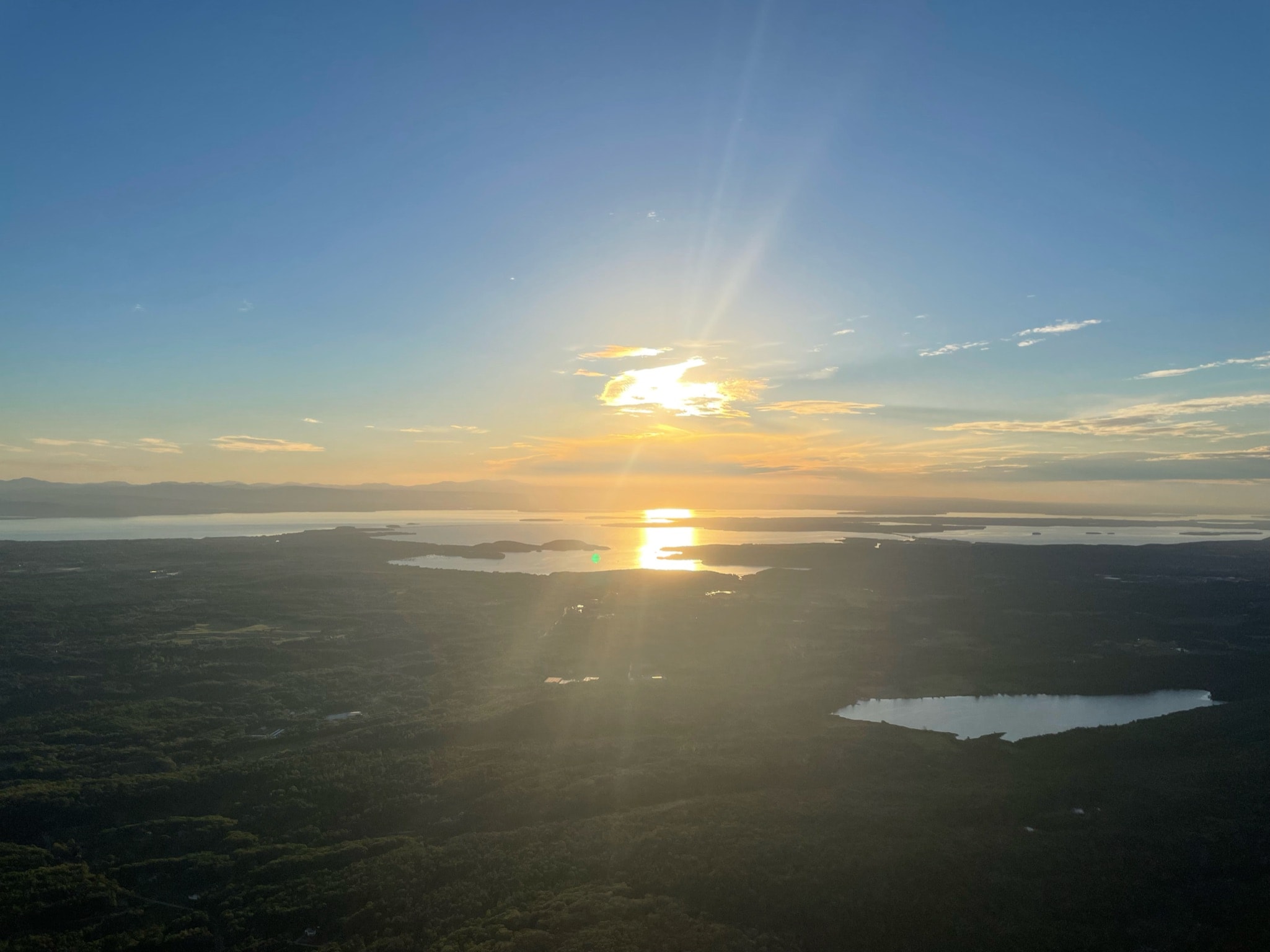 The sun rises in the sky as its reflection glistens in the clear water below. 