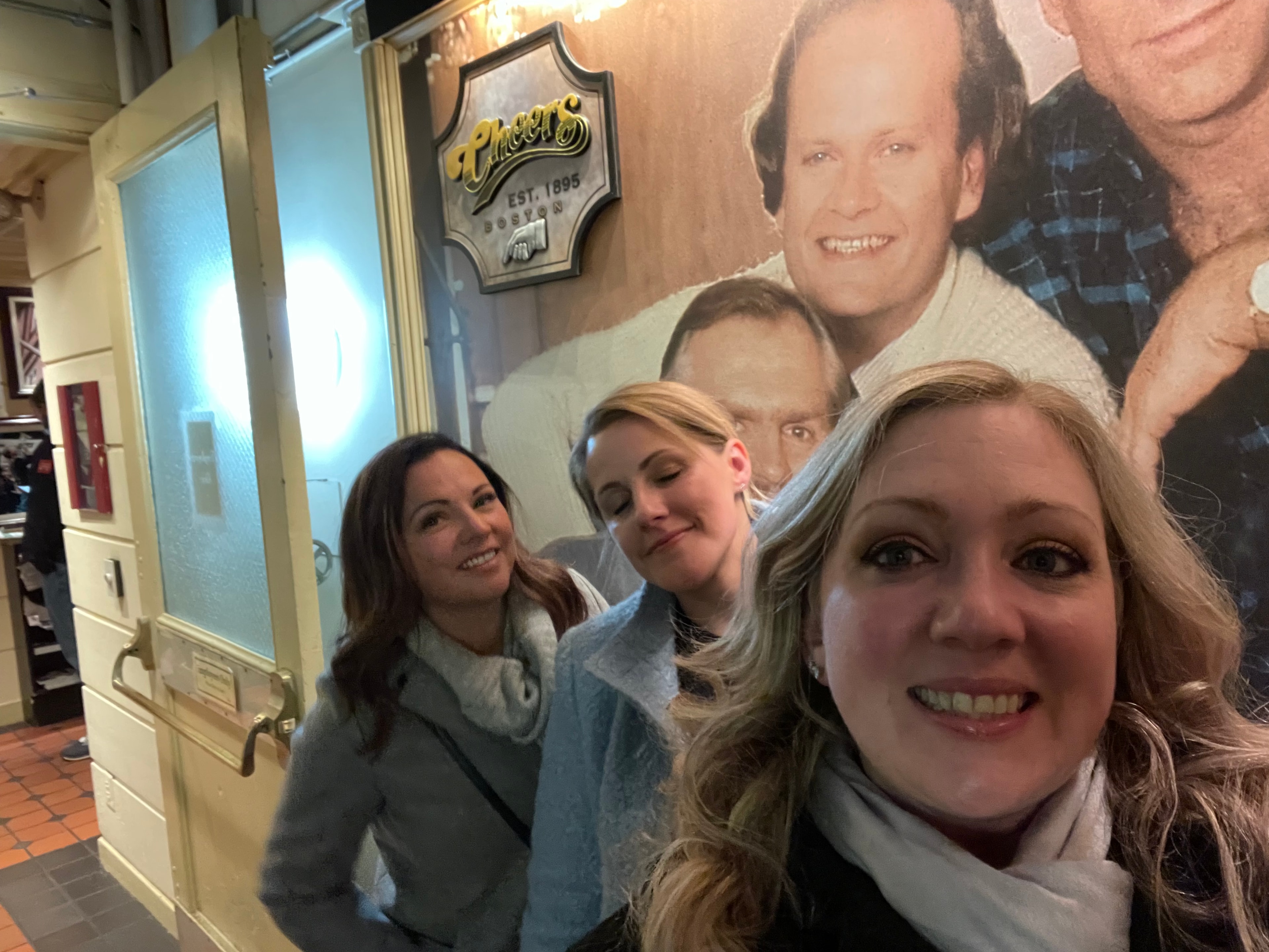 Advisor and friends taking a selfie indoors with a mural of the cast of Cheers behind them