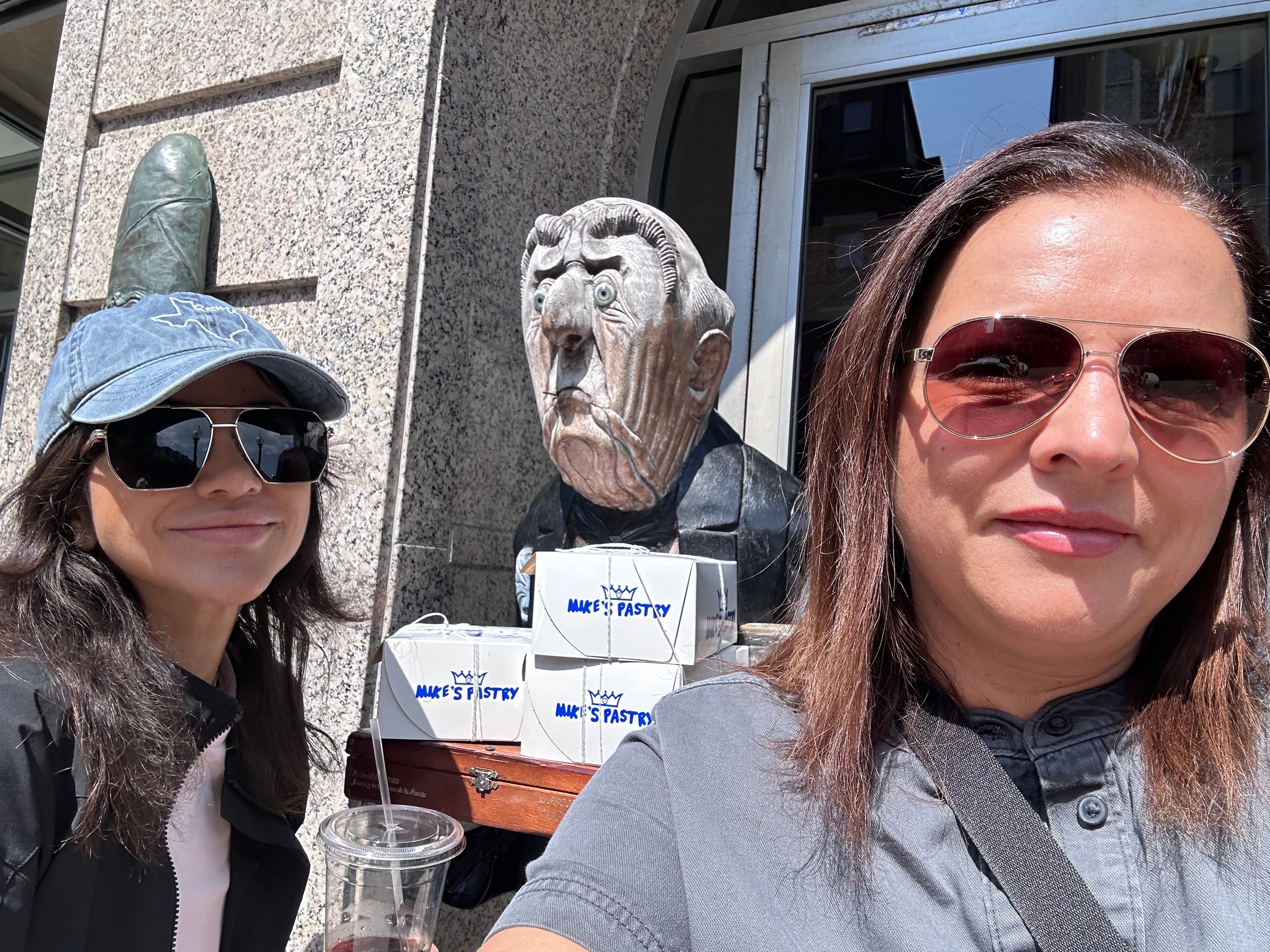 Advisor and another woman both in sunglasses taking a selfie with the stone sculpture of a face on a sunny street