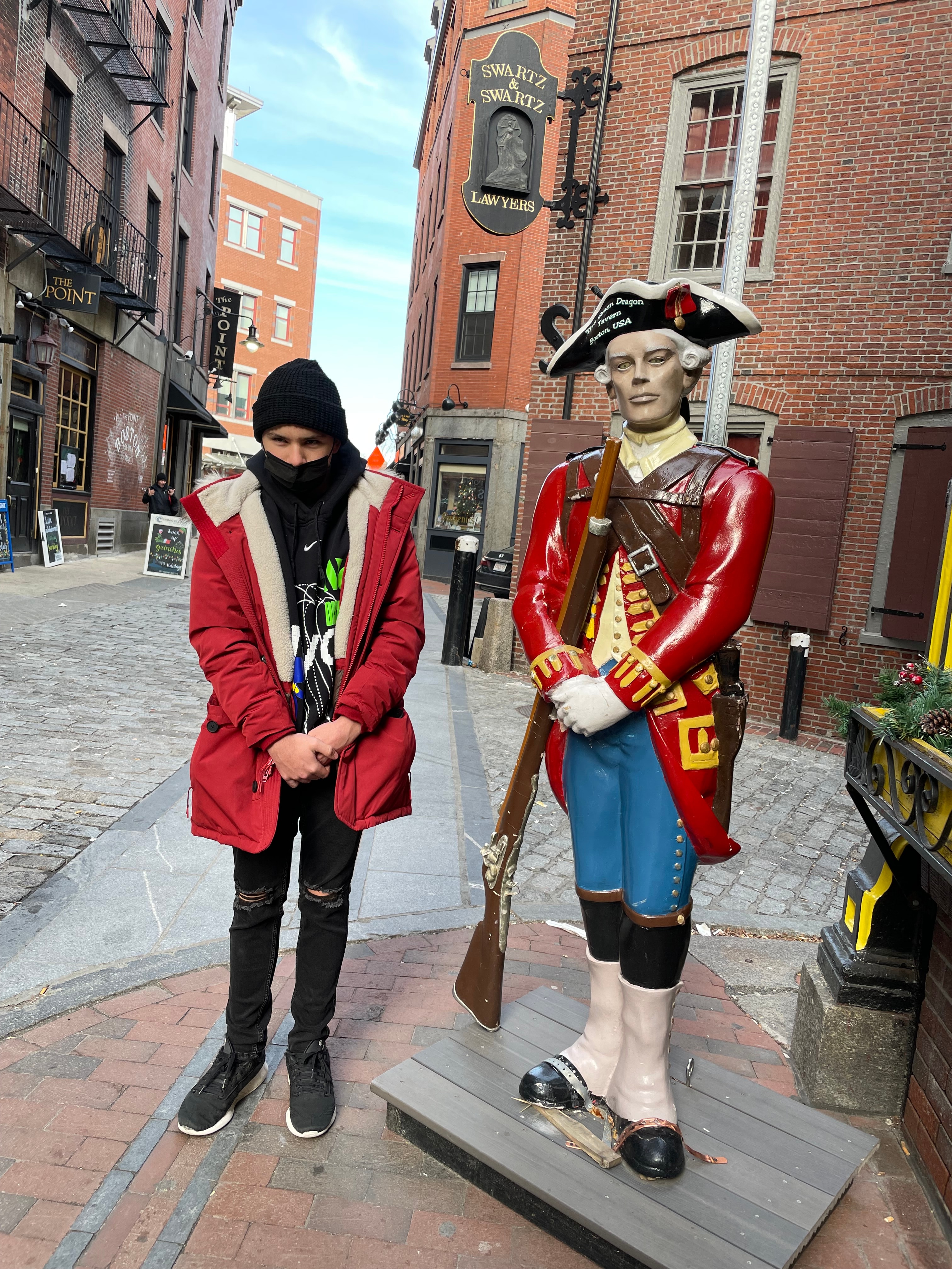 Advisor in a red coat posing beside a human figure of a British red coat soldier on a city street