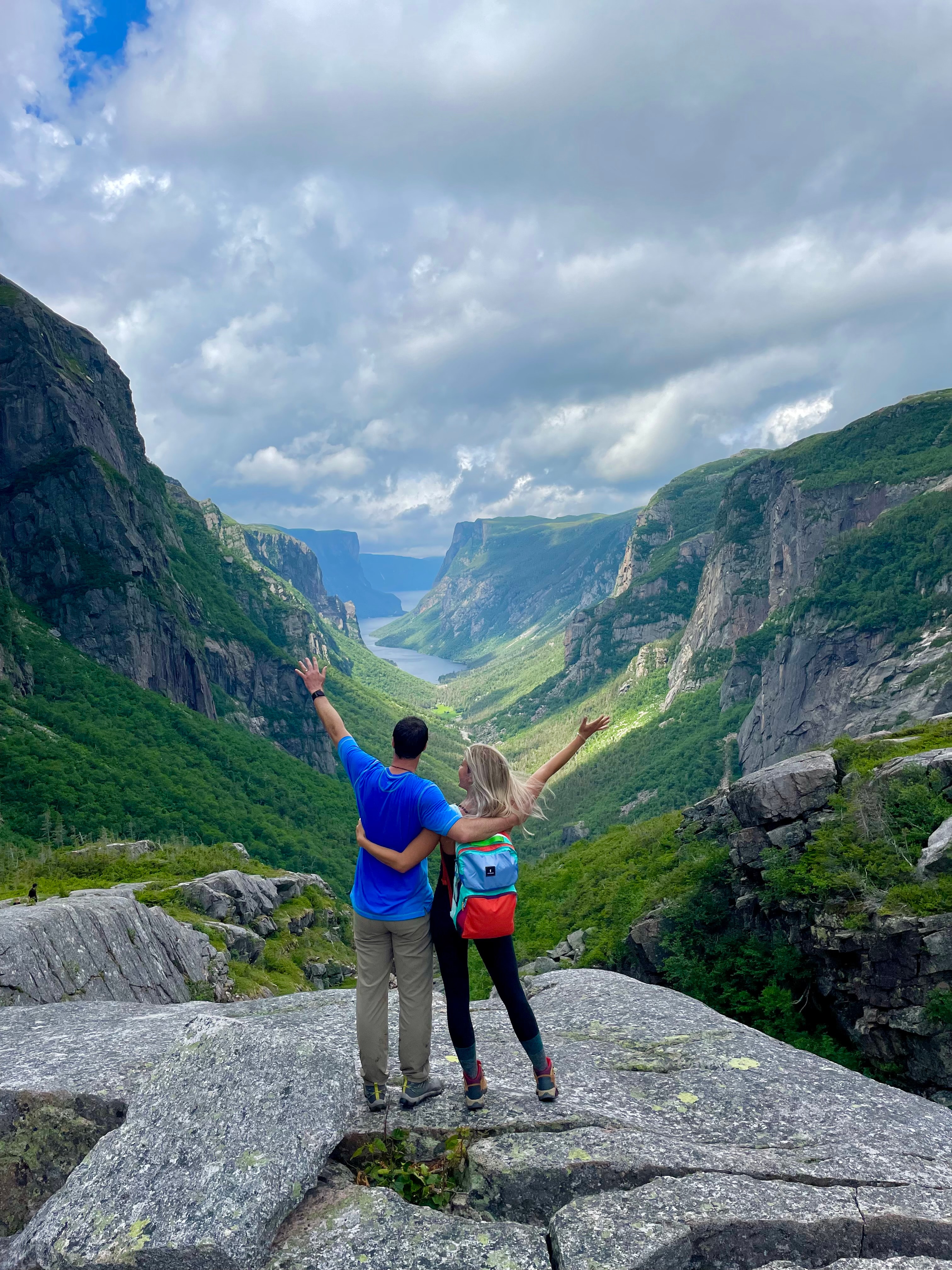 Natalie posing with friend on top of a cliff with the mountains in the background during the daytime.