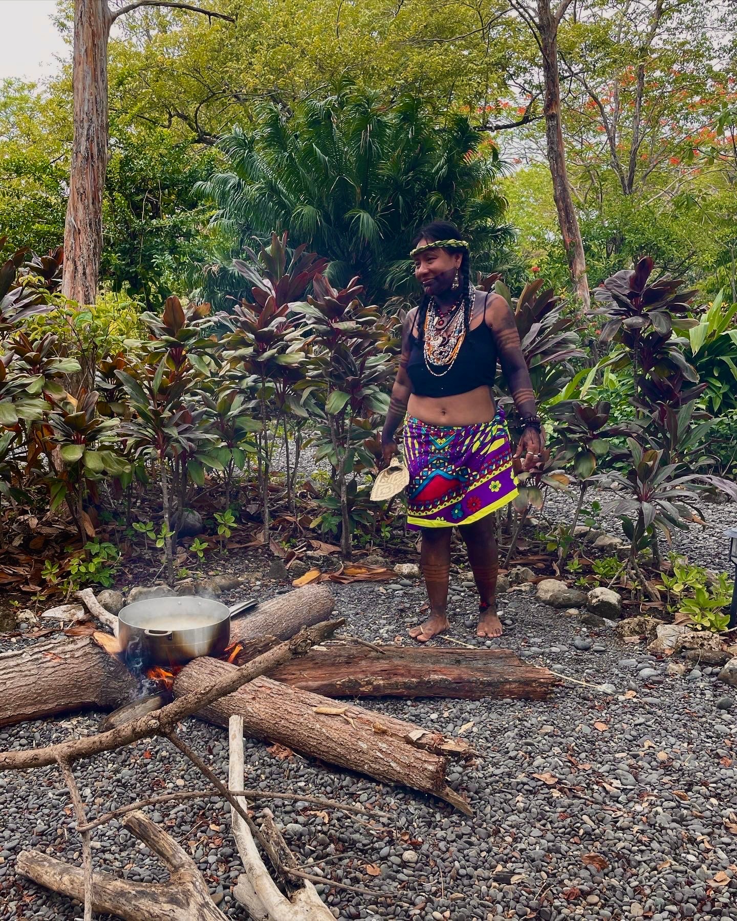 View of a woman cooking in a large pot over a fire in the jungle