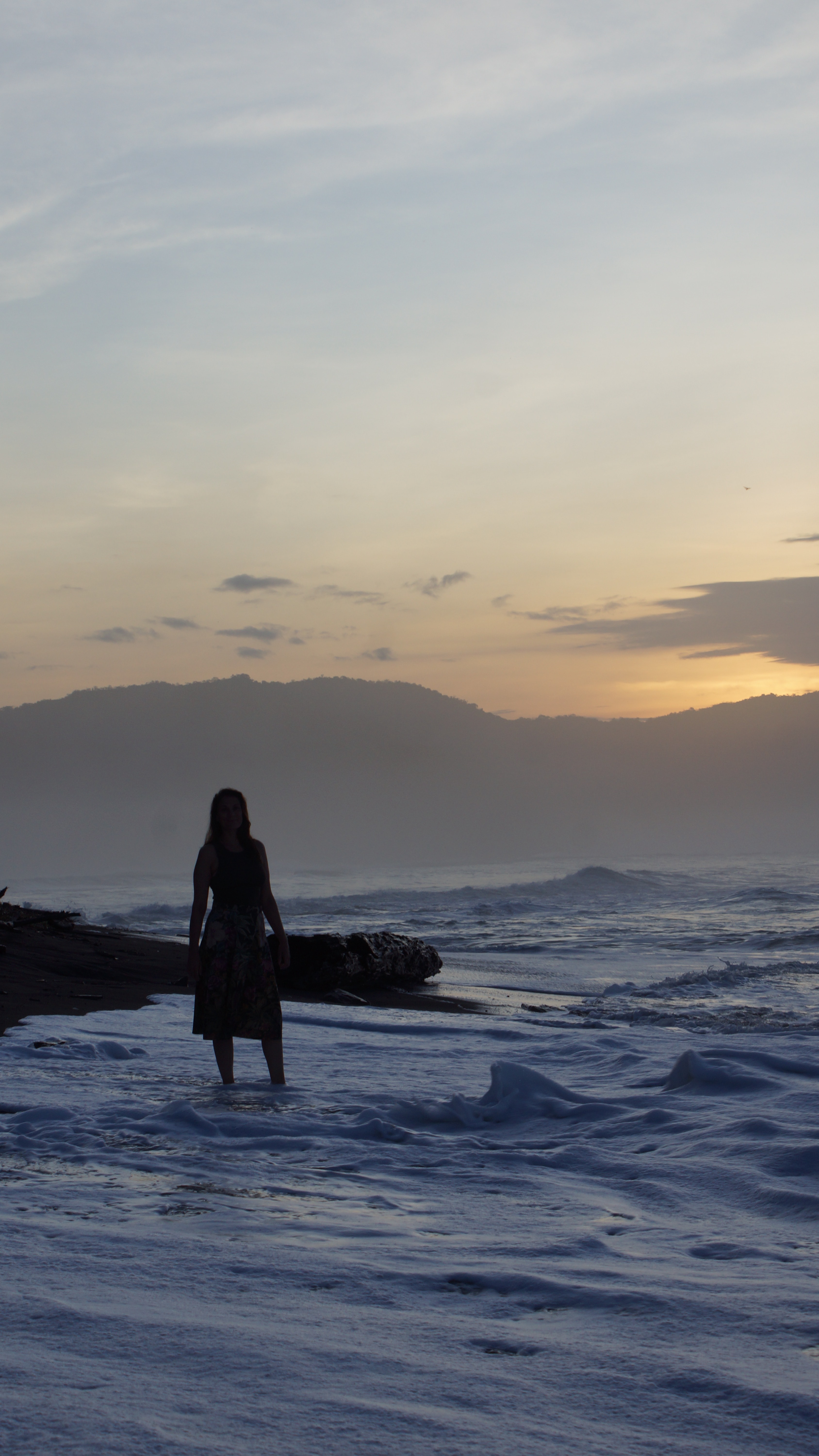 A person in silhouette standing in shallow ocean water at sunset