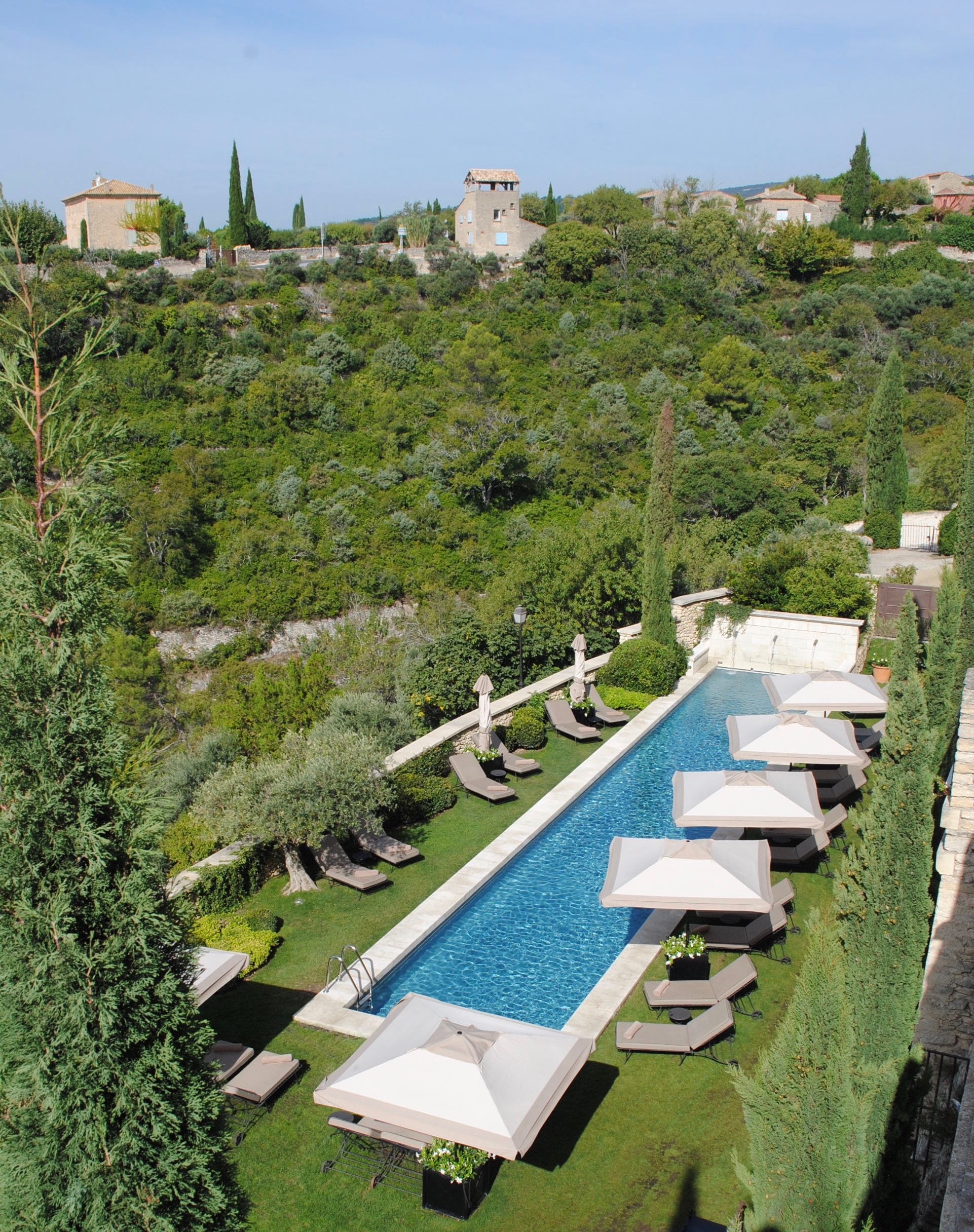 View of a long rectangular resort pool in a green area with lounges and umbrellas to either side