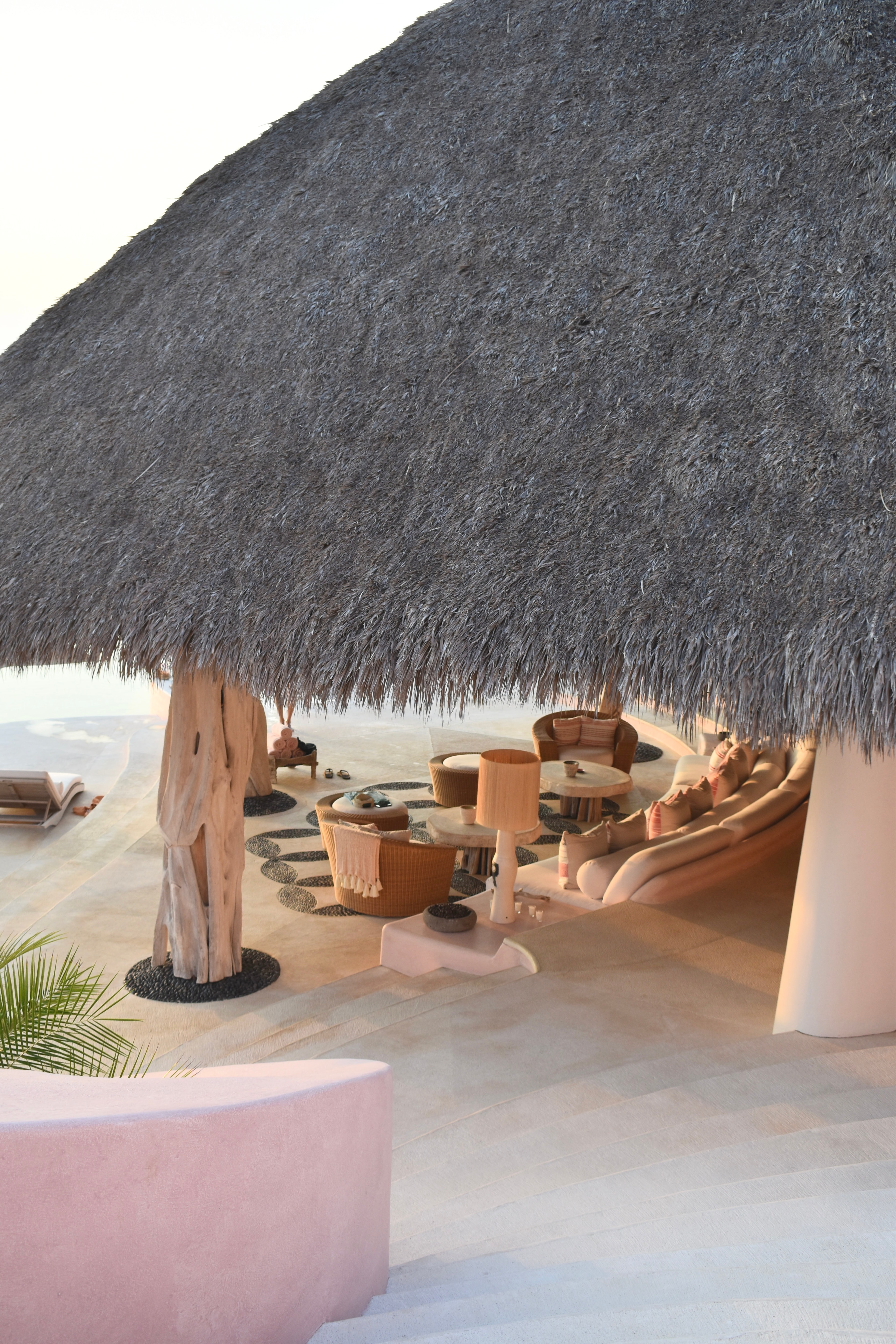 Chairs and couches in a sandy area under a large thatched roof 