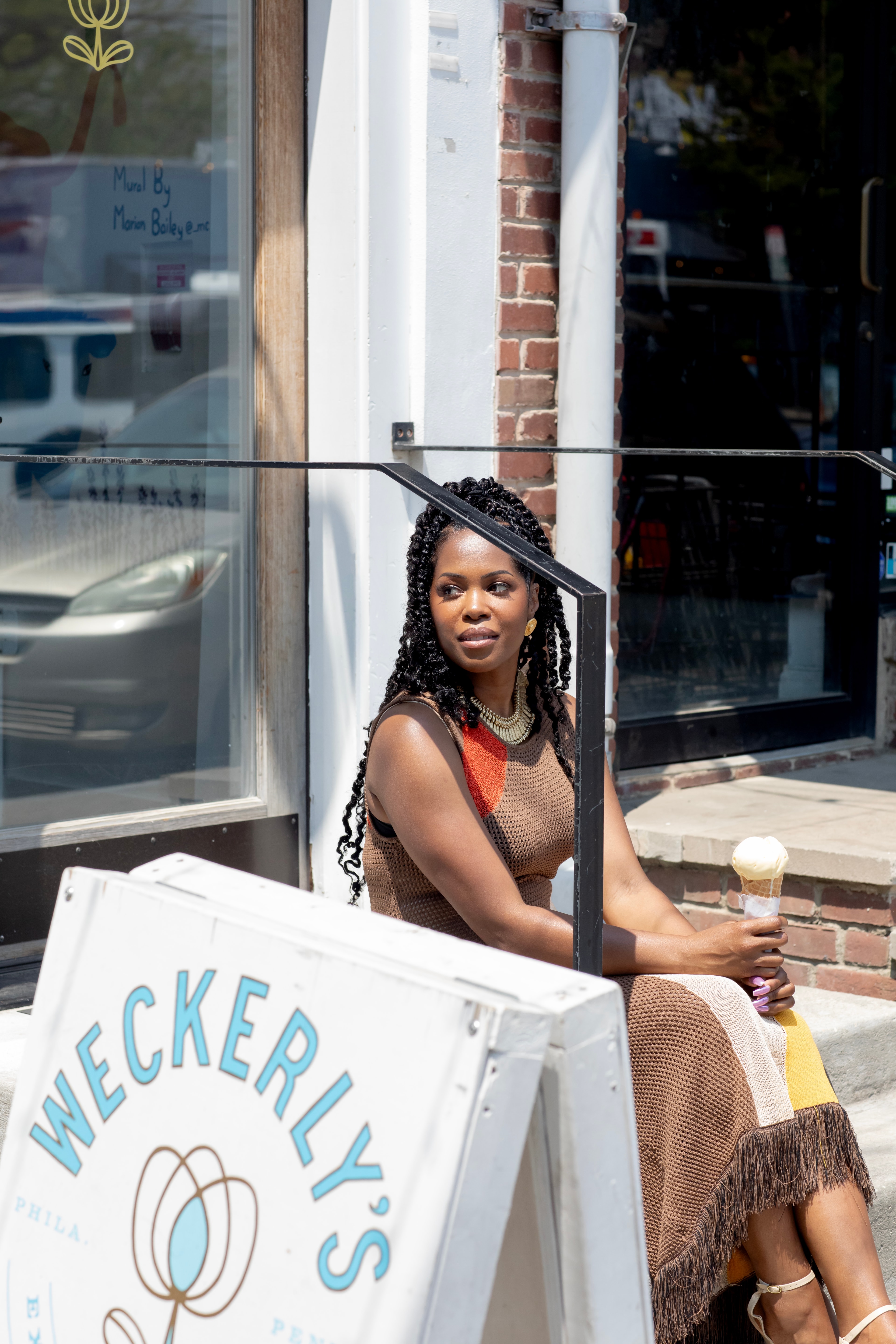 Advisor sitting on steps in front of a shop holding an ice cream cone on a sunny day